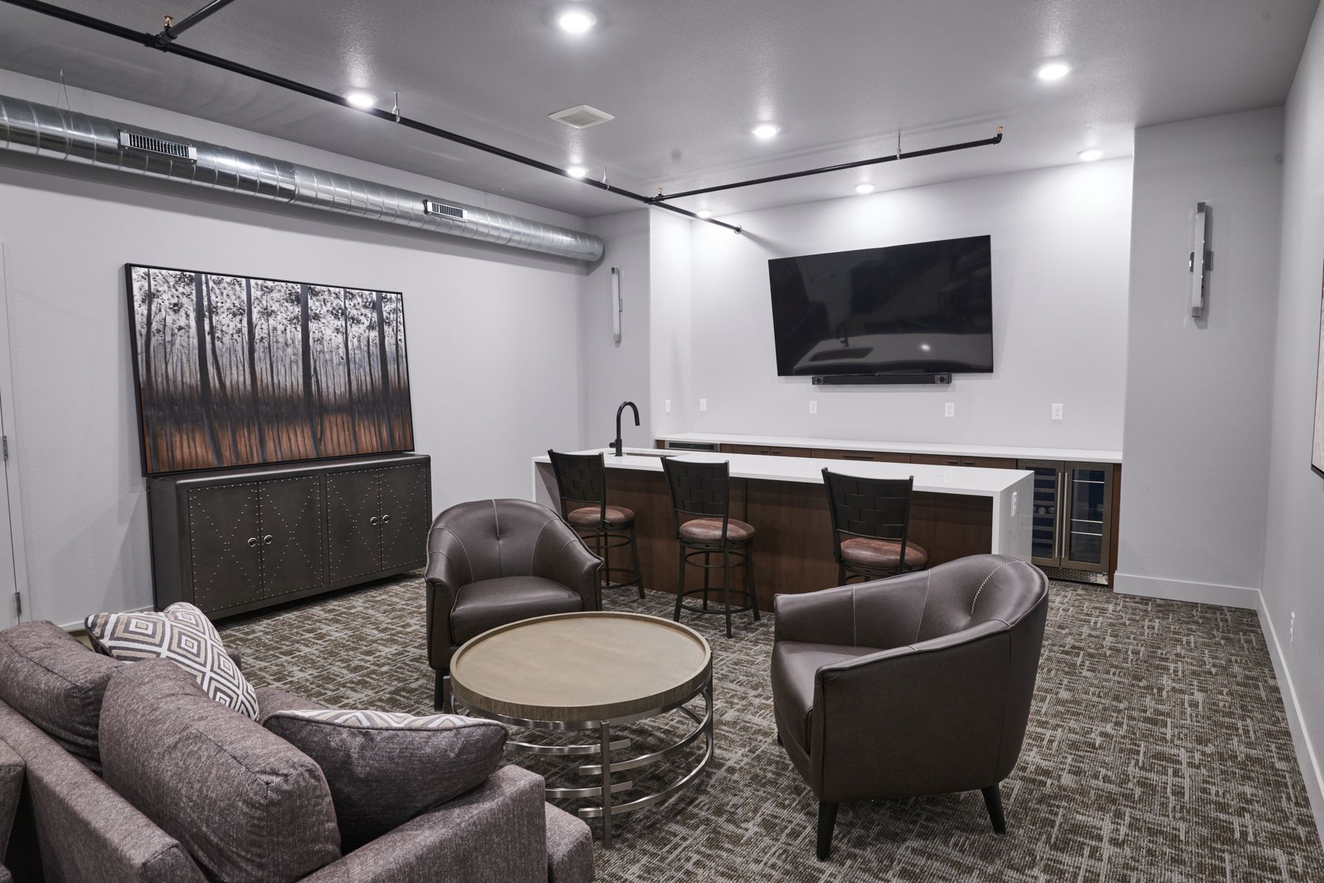 Modern lounge with gray chairs, round table, TV, and bar seating in a white room