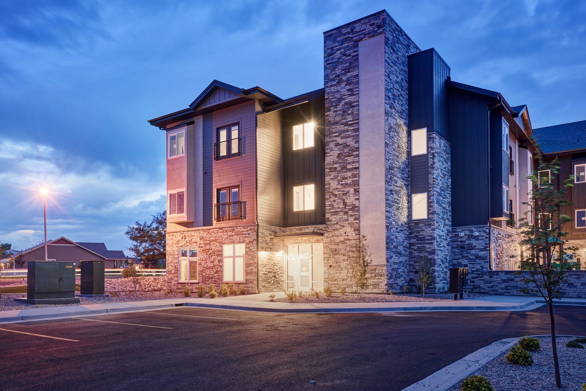 Modern apartment building at dusk with stone accents and warm lights glowing from windows