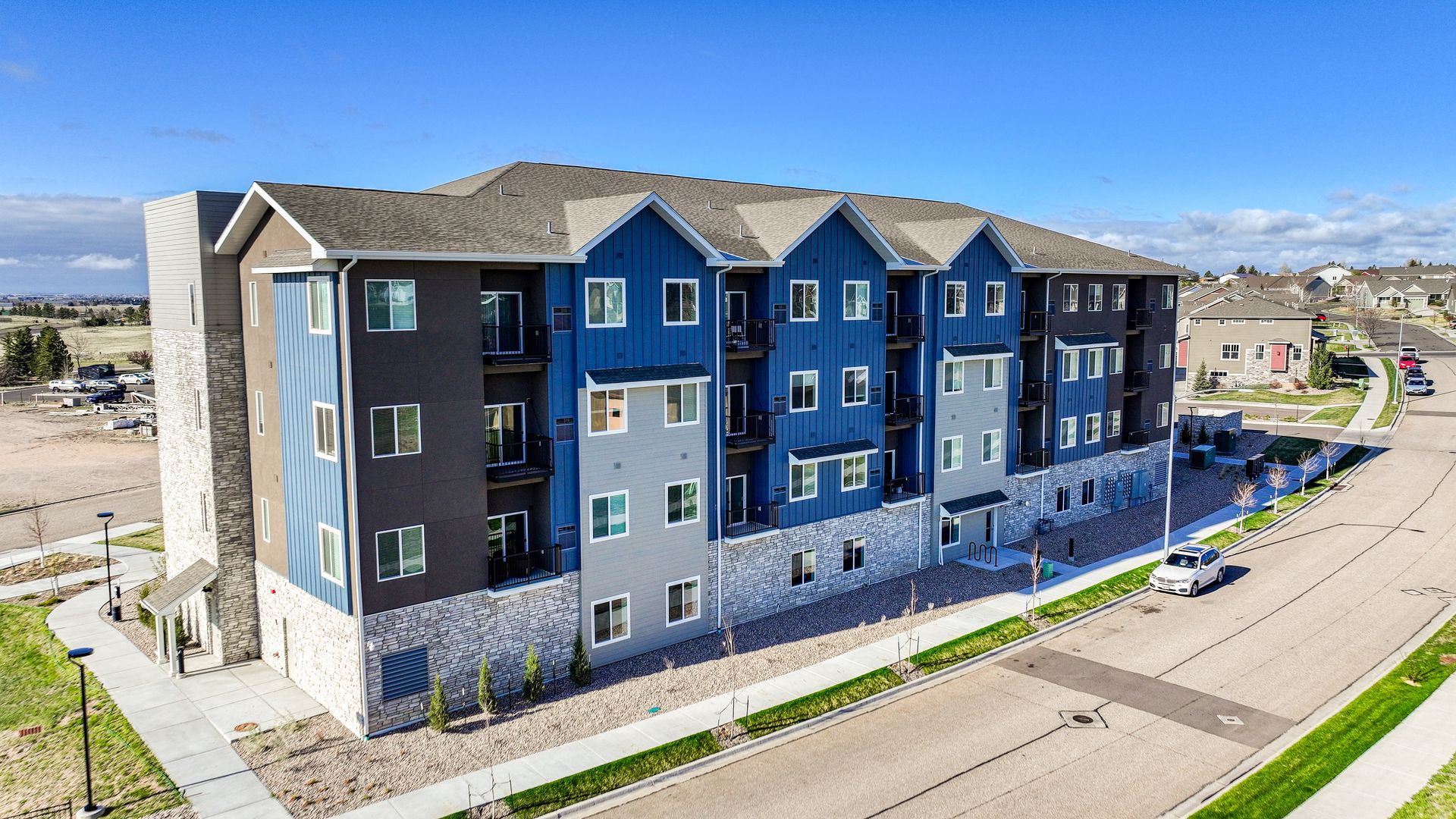 Modern blue-and-gray apartment building along a curved street on a sunny day
