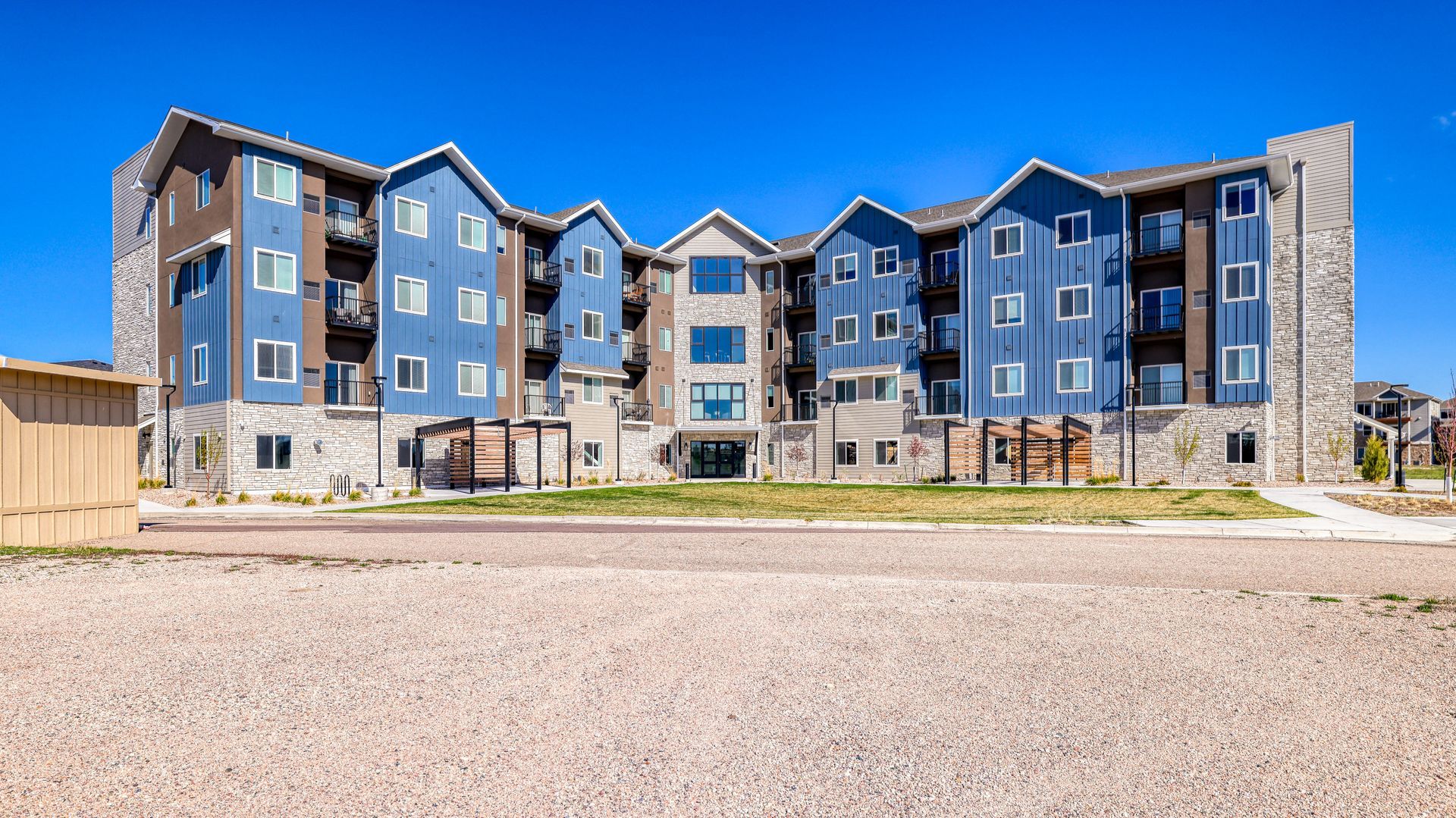 Modern blue-and-gray apartment building with stone accents under a clear blue sky