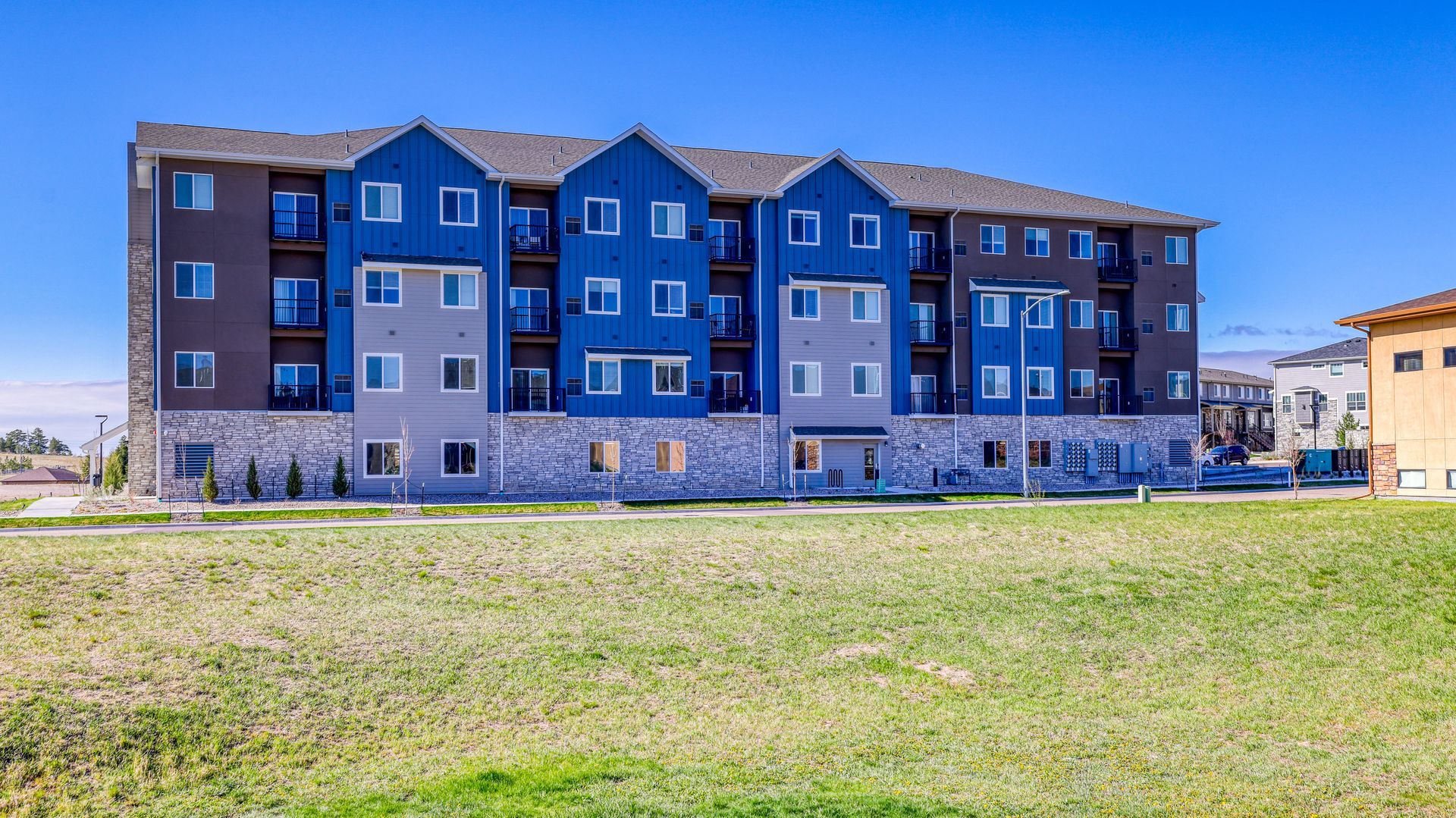 Blue apartment building with balconies behind a grassy field under a clear sky
