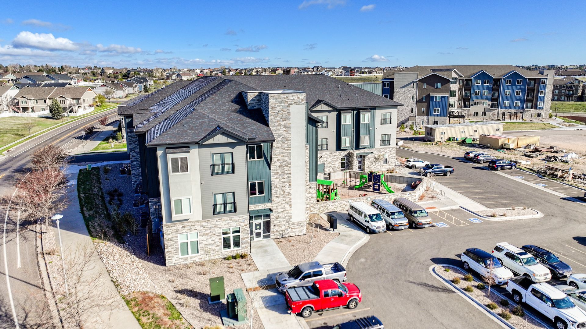 Aerial view of a modern apartment complex with parked cars and surrounding residential buildings
