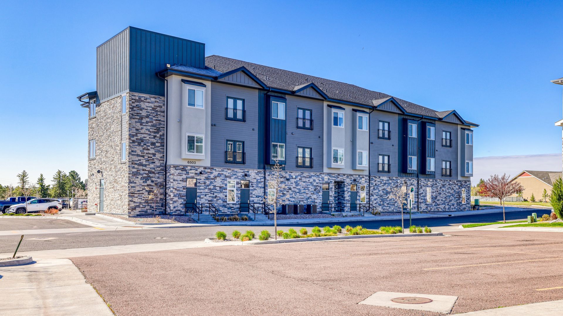 Modern gray stone-and-blue commercial building exterior on a sunny day with a parking lot in front