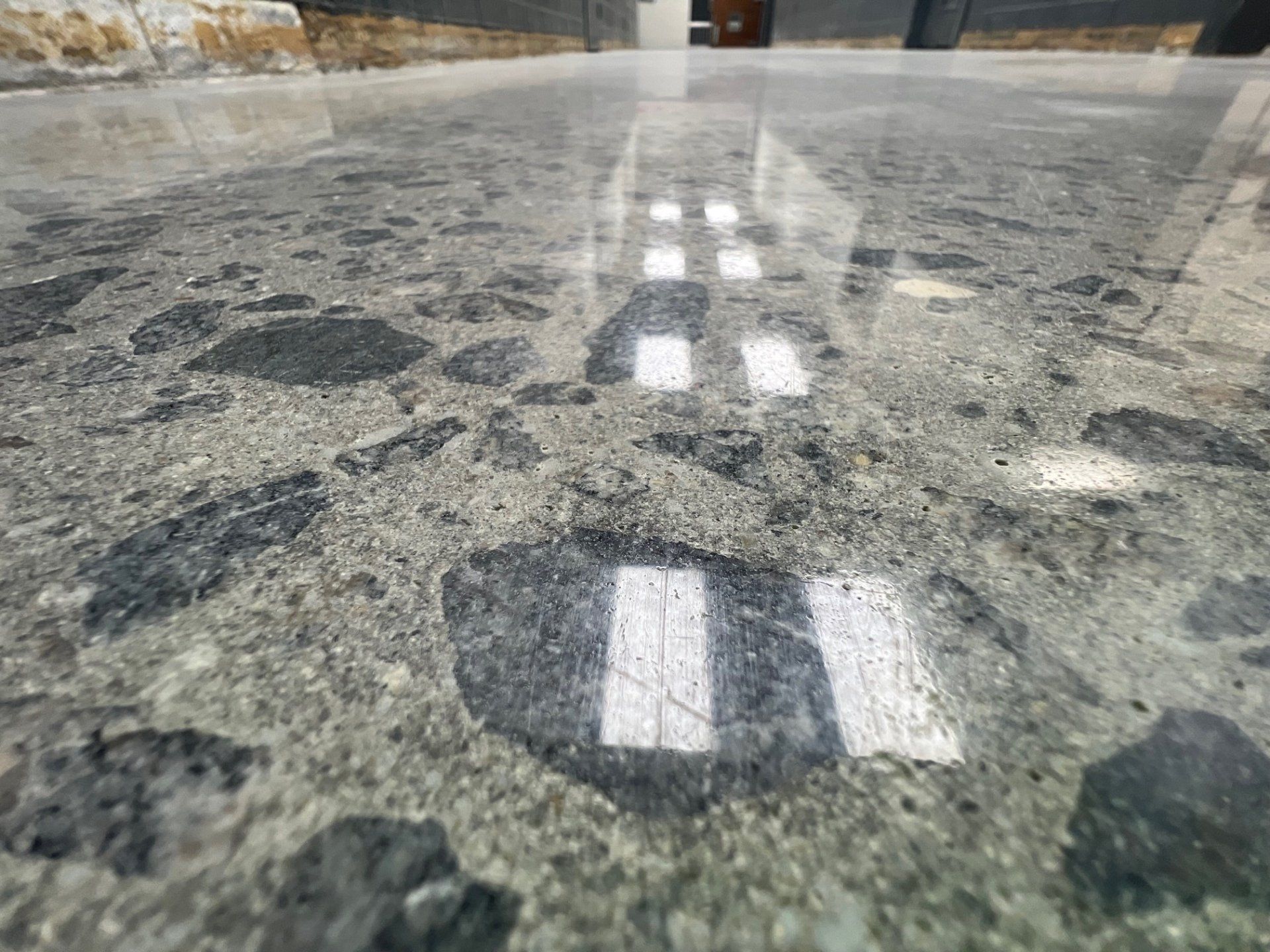 Polished concrete floor reflecting bright rectangles, likely from a light source. Gray and black aggregate.