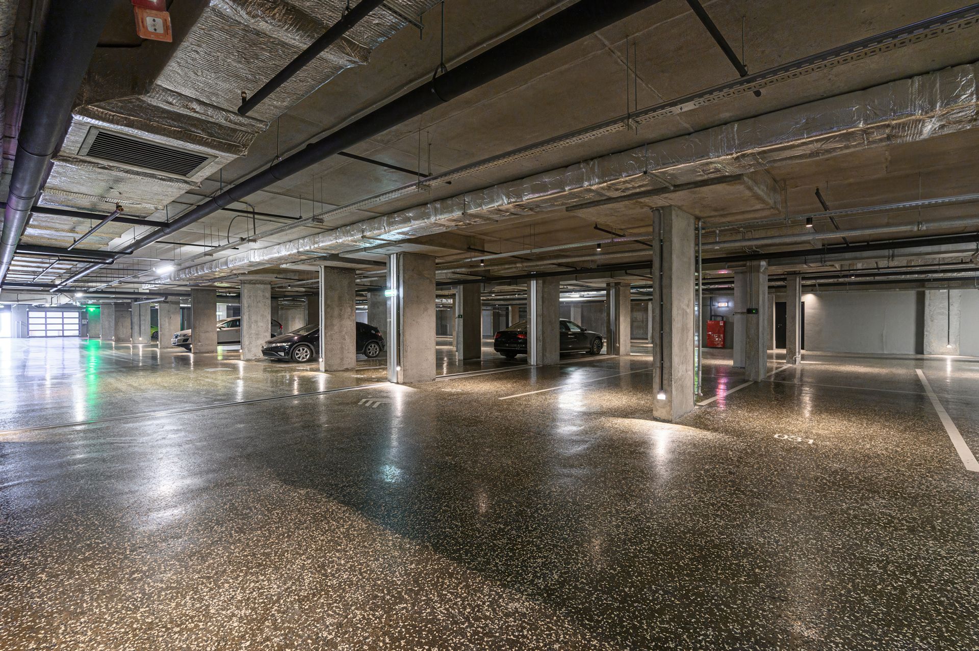Empty underground parking garage with concrete pillars and parked cars.