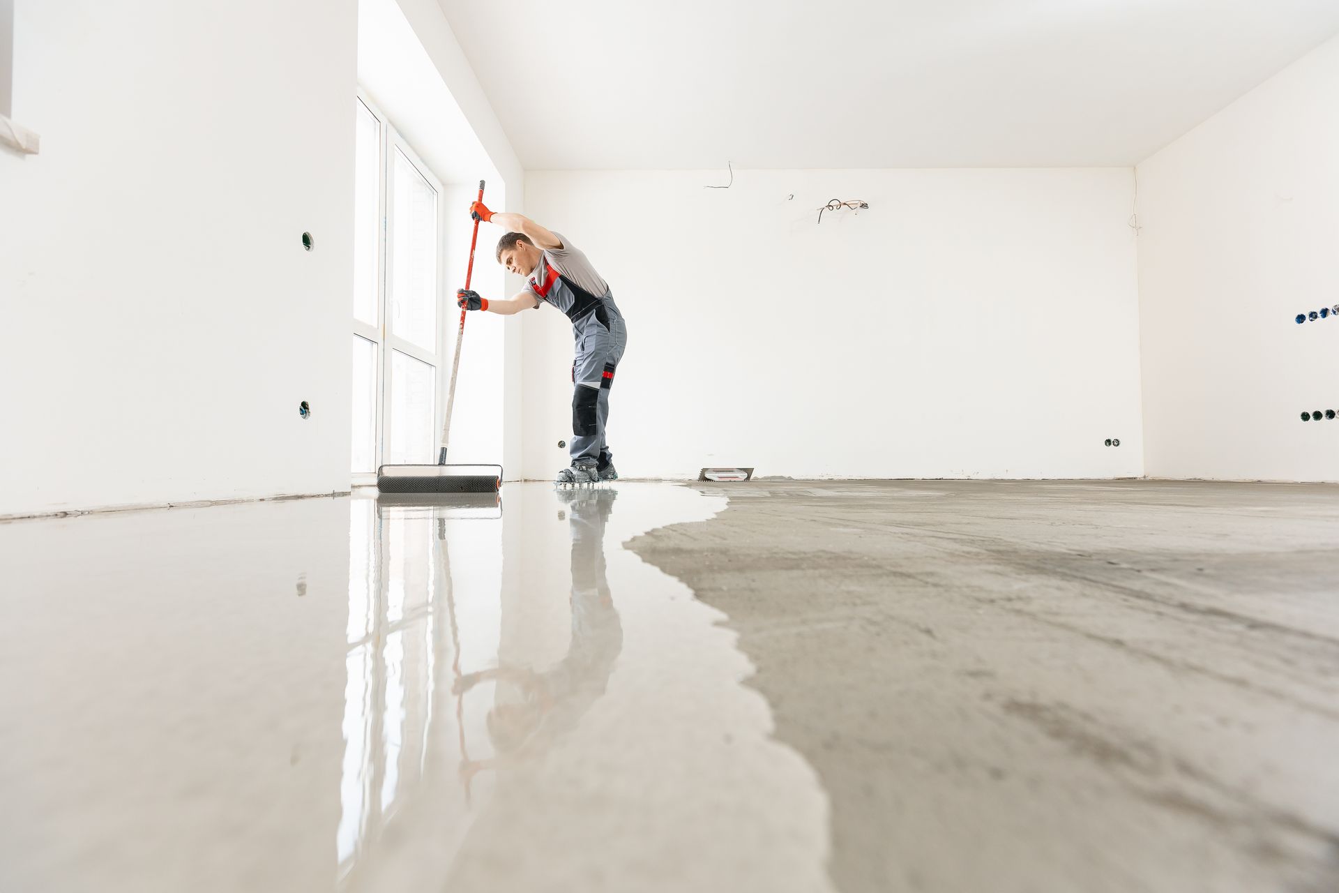 Worker smoothing wet concrete floor in a bright empty room