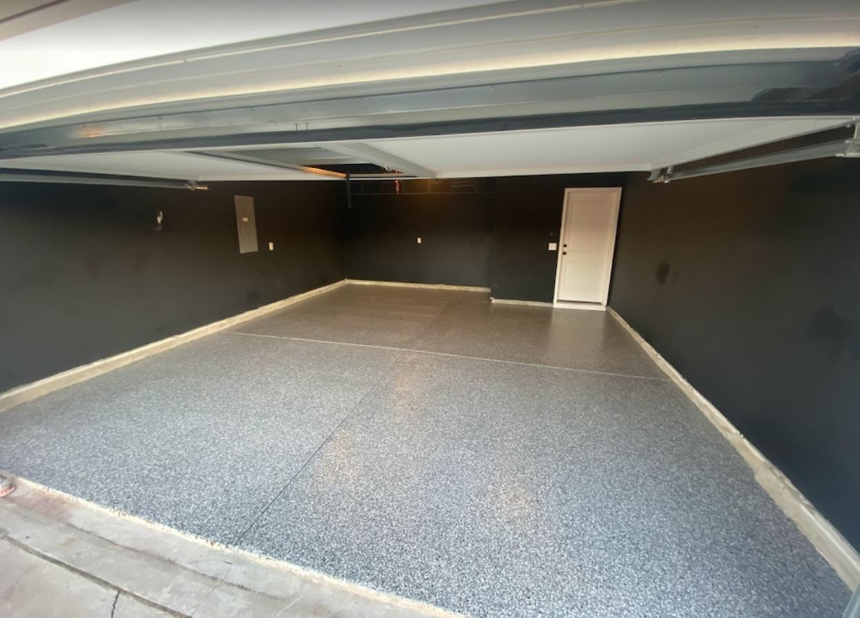 Empty garage interior with grey speckled floor and dark grey walls; white door.