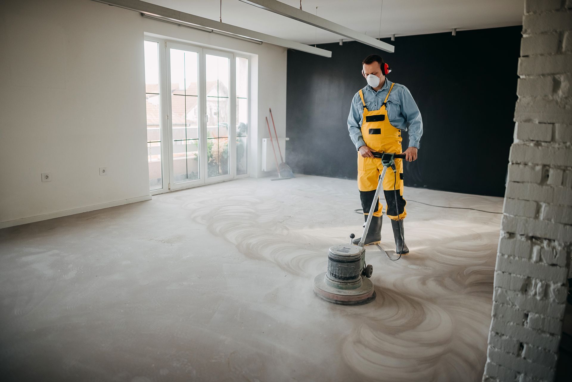 Worker in yellow overalls polishing a concrete floor with a floor grinder.