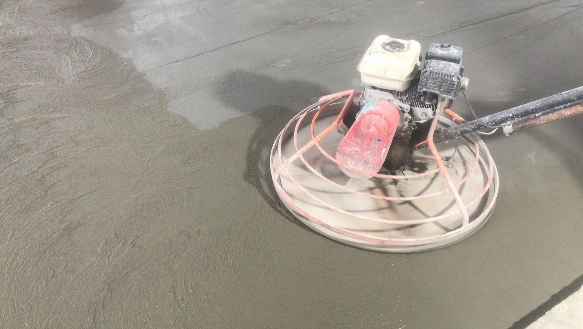 Power trowel smoothing wet concrete surface during construction.