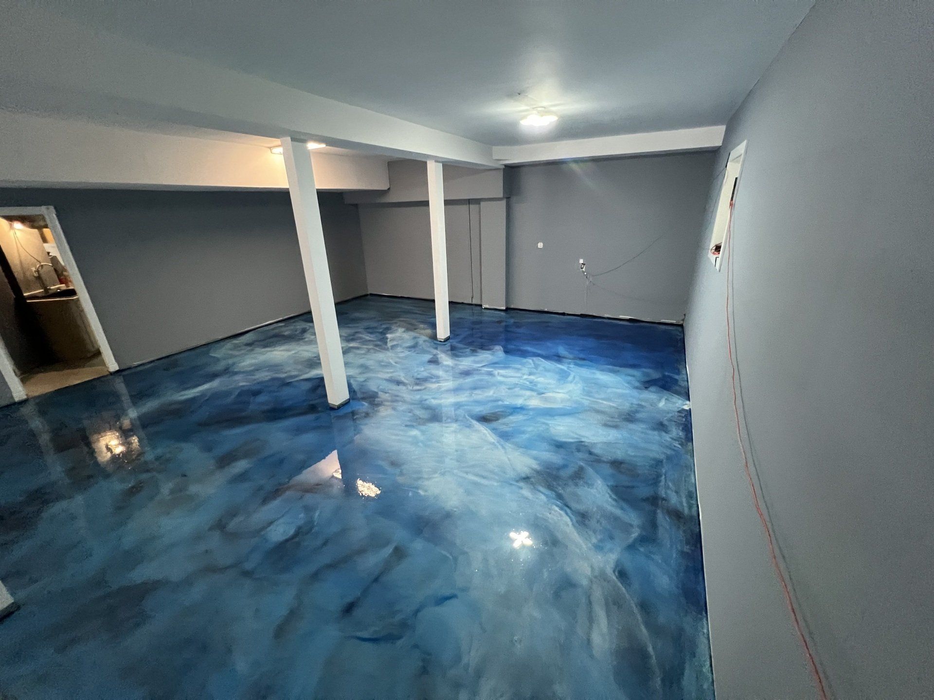 A room with a blue and white swirled epoxy floor and gray walls. Two white support beams stand in the center of the room.