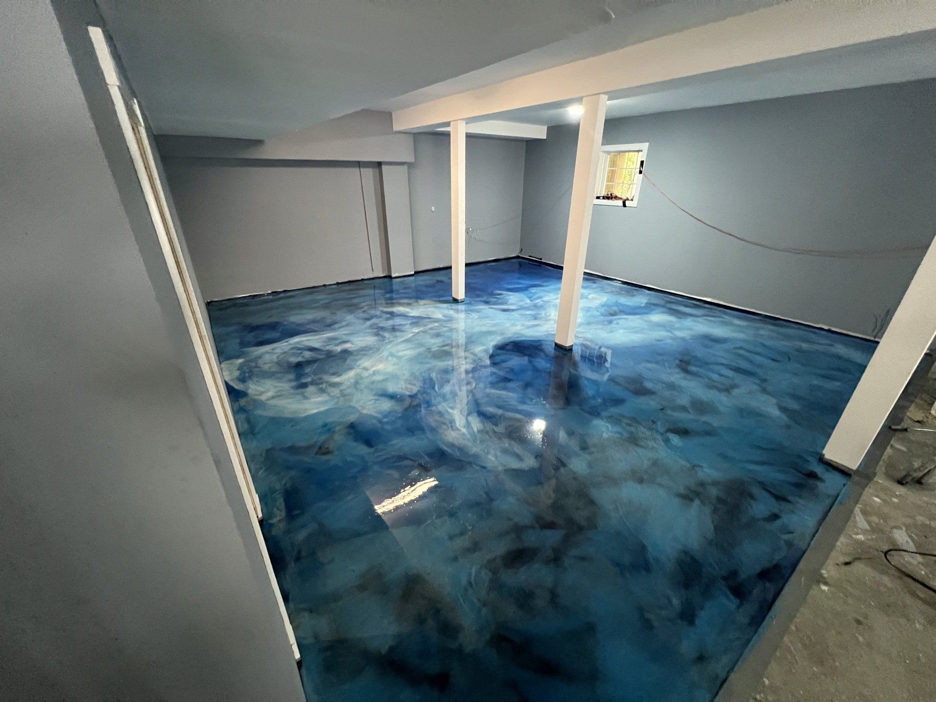 Blue and silver epoxy flooring in a room with gray walls and white support beams.