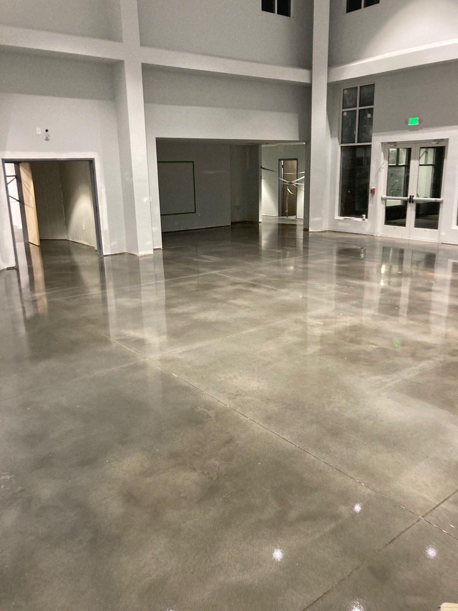 Spacious room with polished gray concrete floor reflecting light. White walls, pillars, and doorways create an open interior.