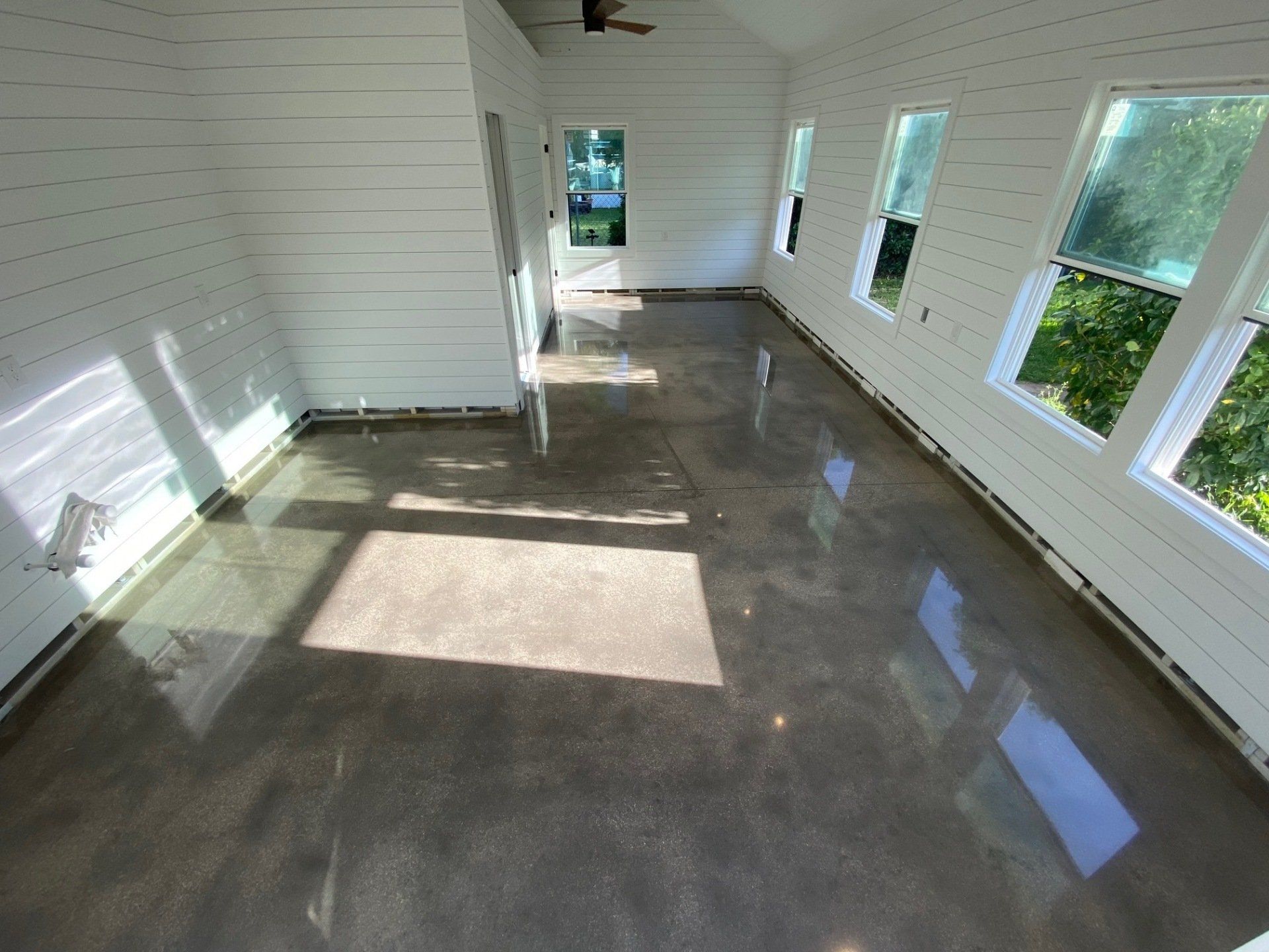 Sunroom with shiny, polished concrete floor, white shiplap walls, and windows with tree views.