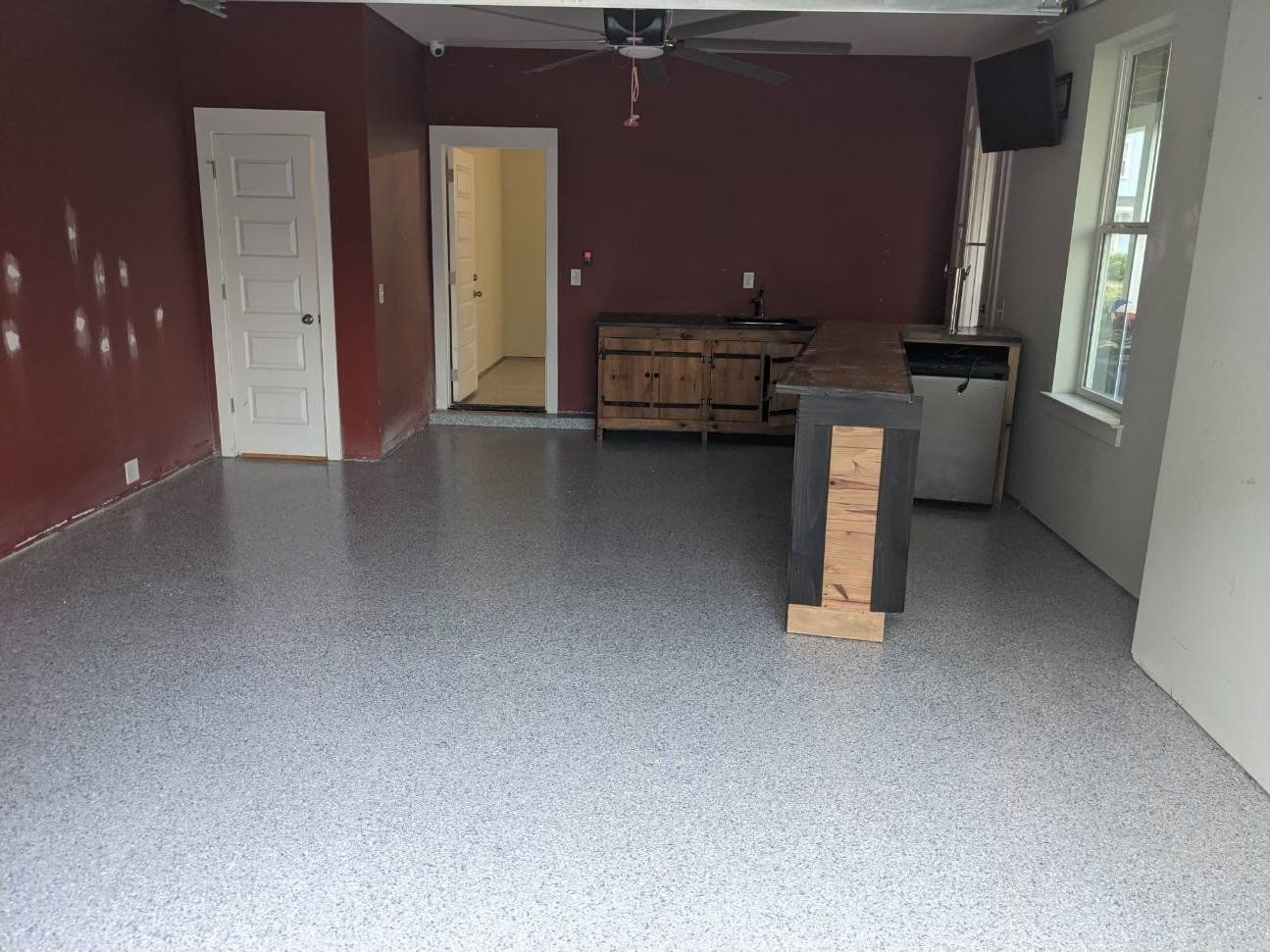 A remodeled garage with a gray speckled floor, burgundy walls, and a wooden counter. 