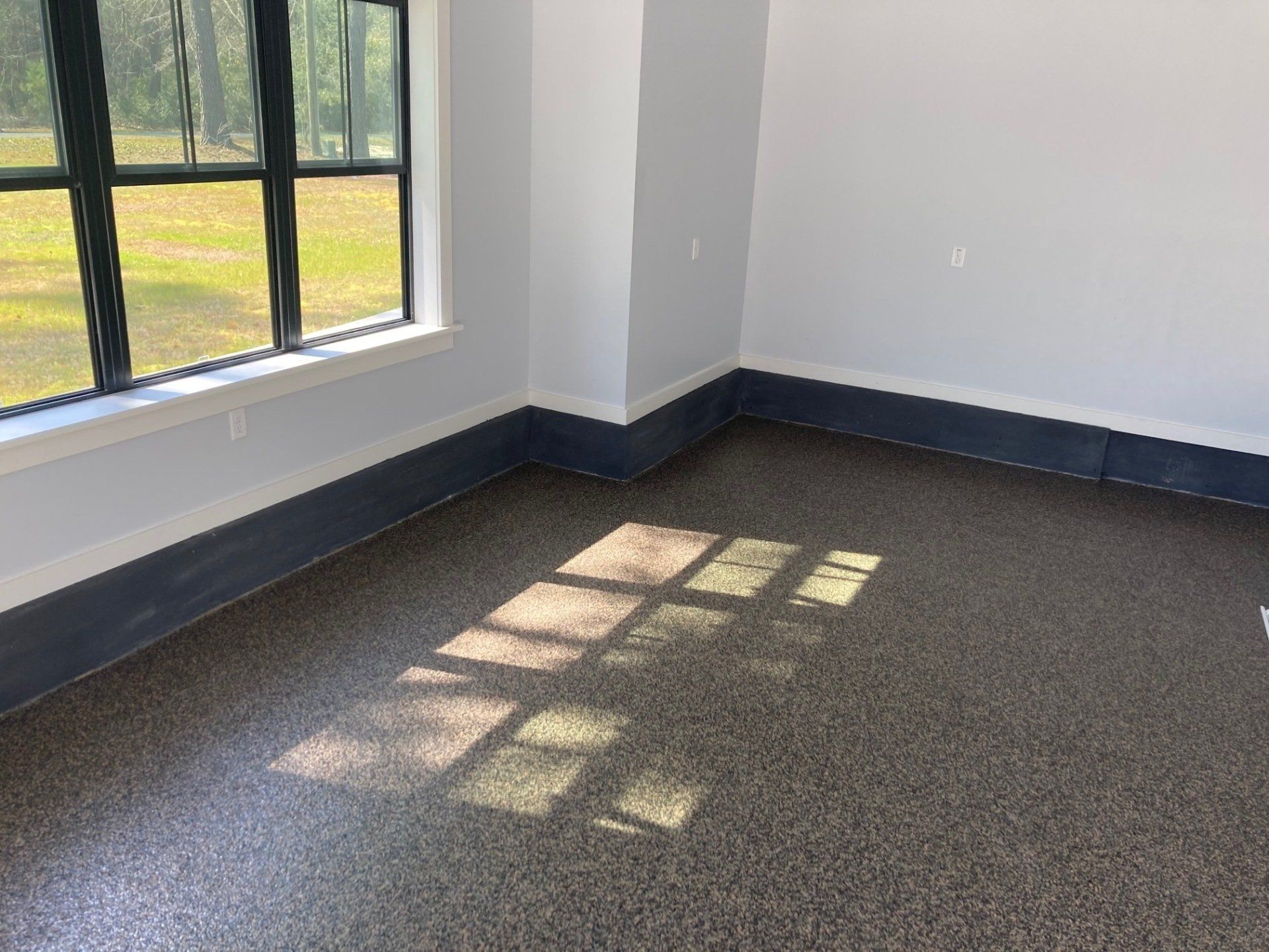 Interior of a room with a speckled floor, a window, and dark blue baseboards. Sunlight casts a rectangular shadow.