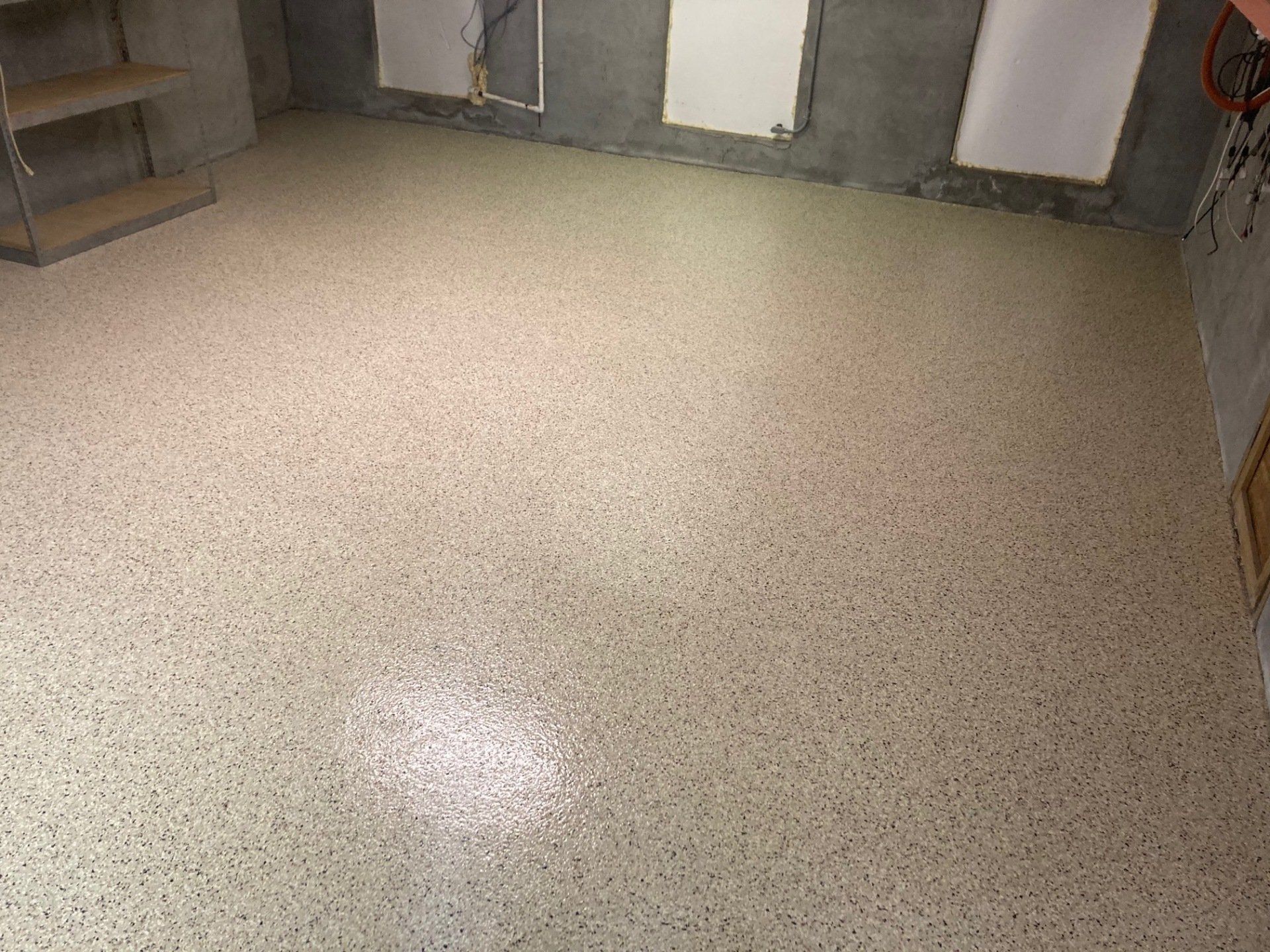 A room with a speckled, light-colored epoxy floor. Gray walls and white window frames surround the floor.