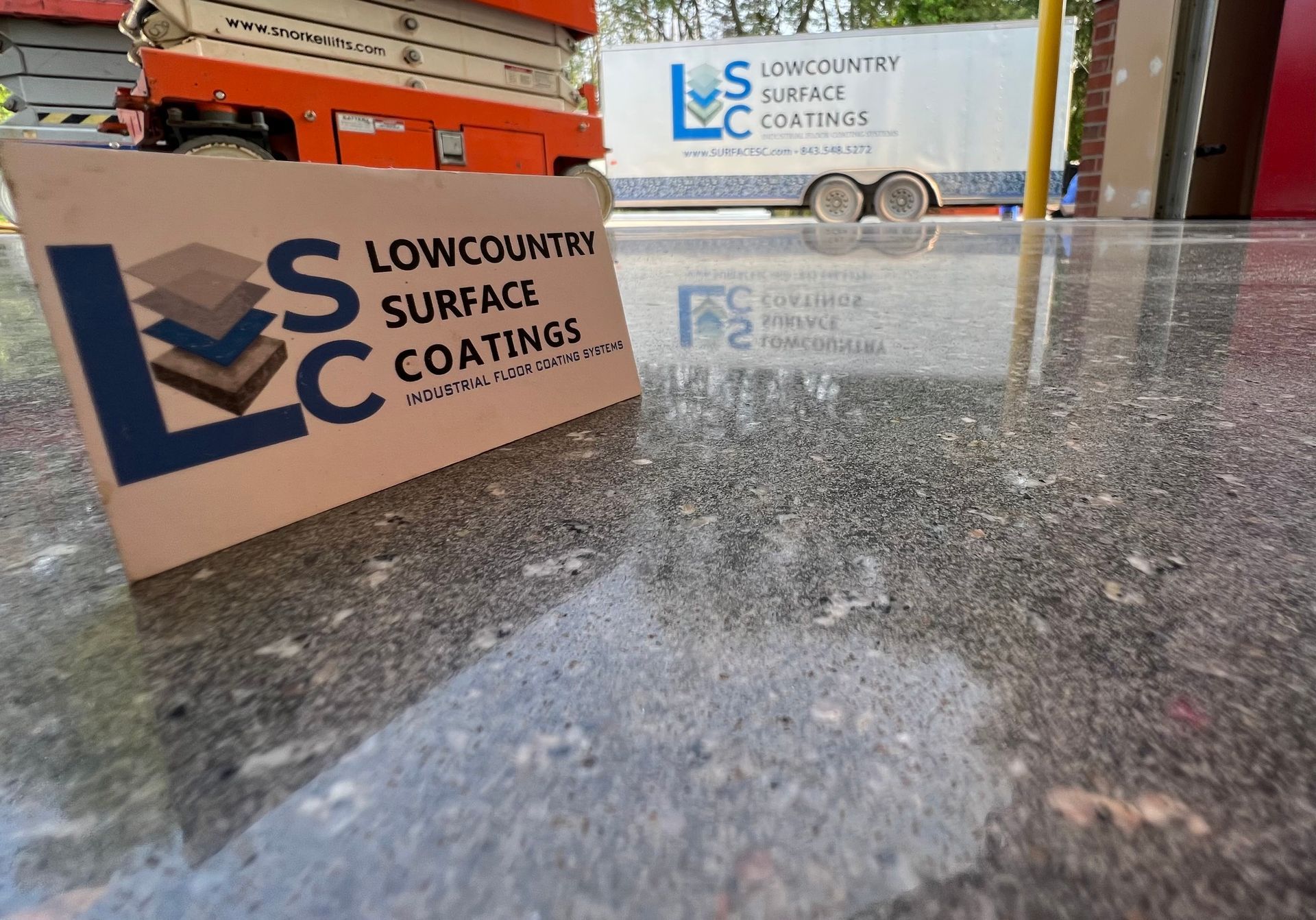 A Lowcountry Surface Coatings sign and trailer in front of a polished concrete floor with an orange lift in the background.