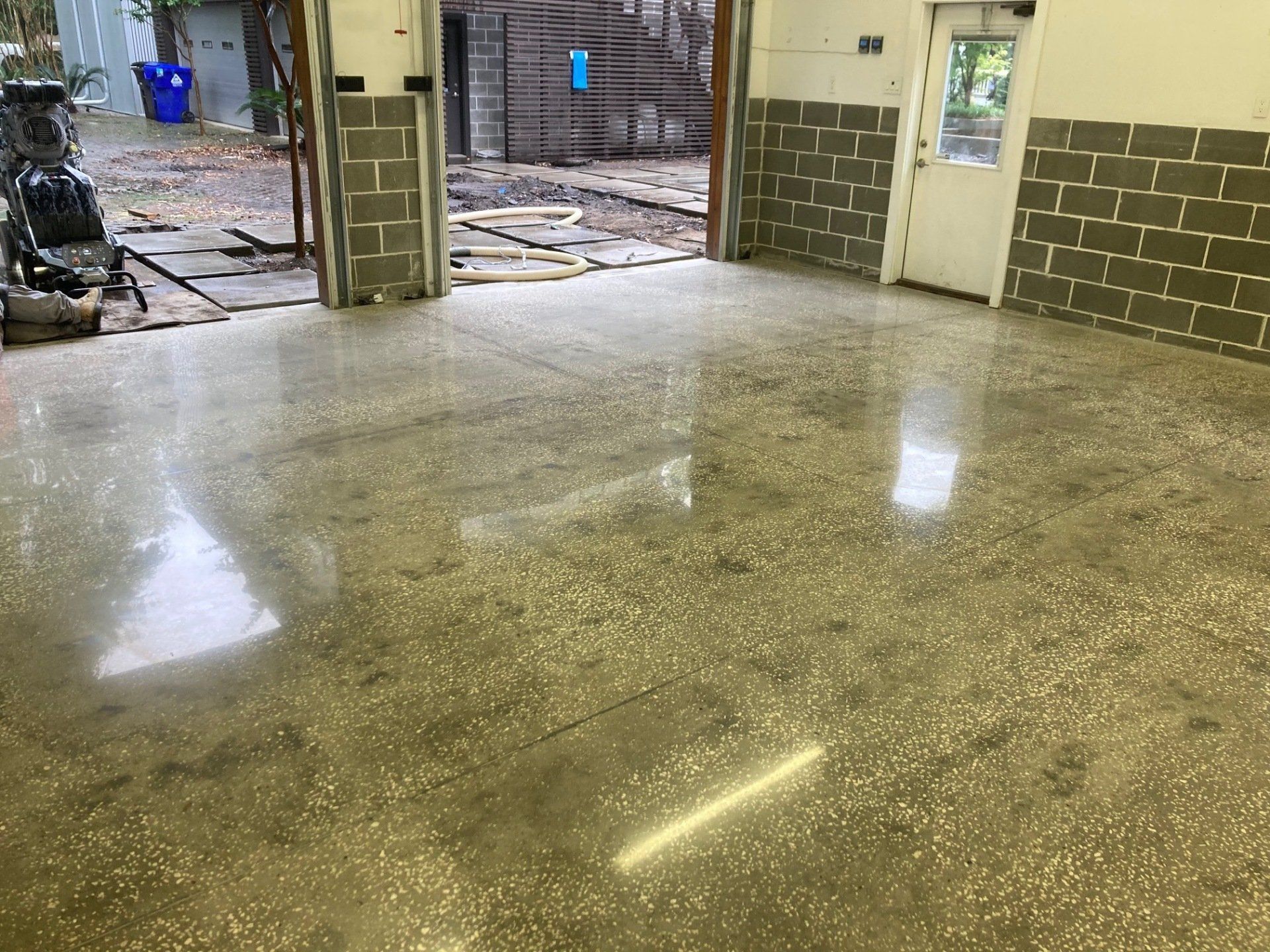A polished concrete floor inside a building, reflecting light. Gray block walls and a door are visible in the background.