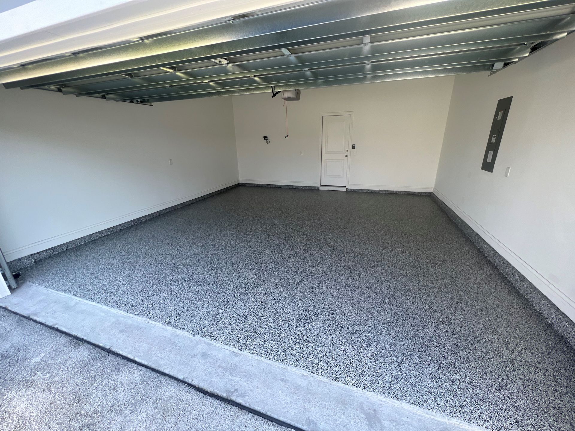 Empty garage with gray speckled epoxy flooring, white walls, and an open garage door.