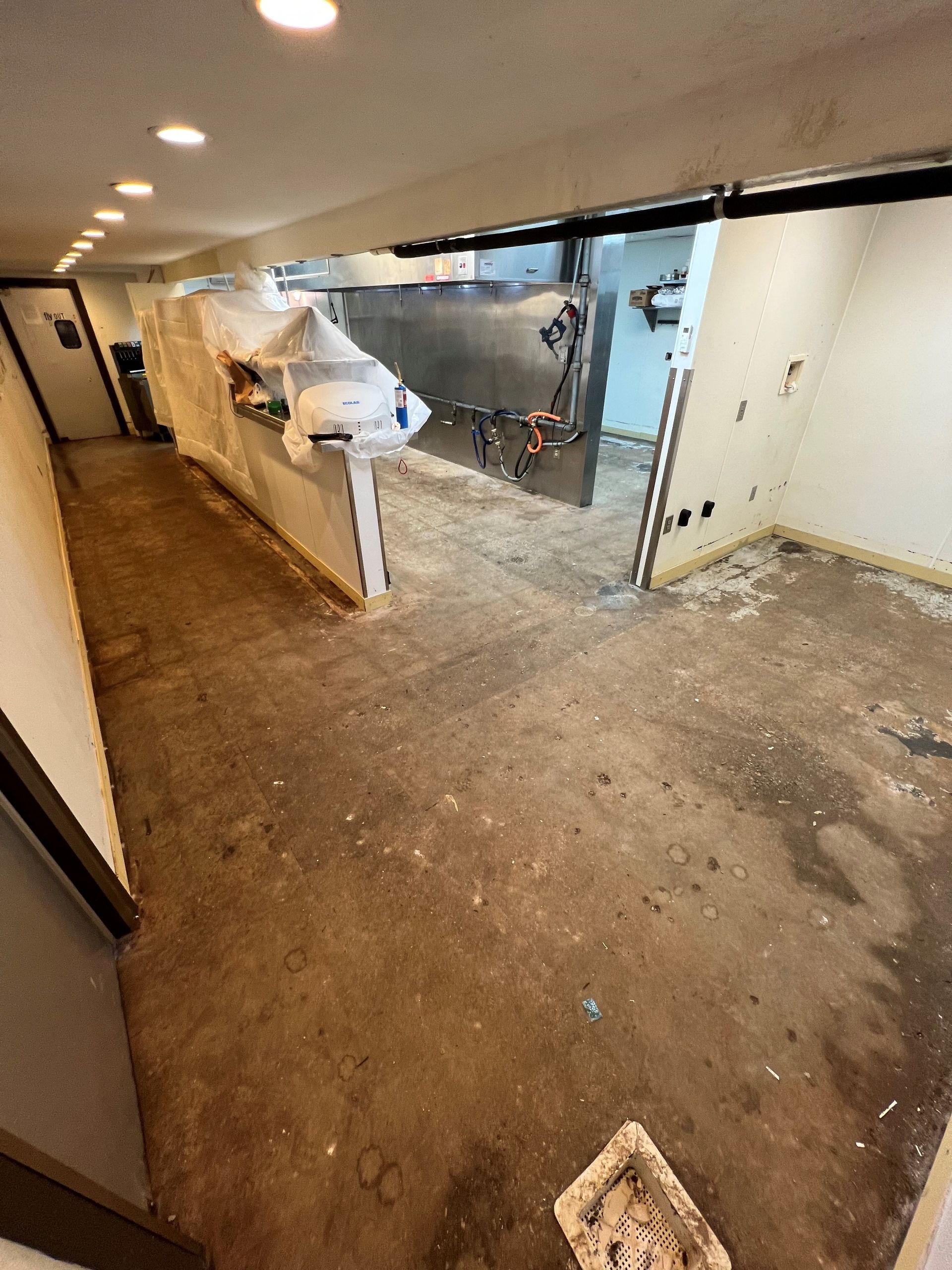 Dirty commercial kitchen under construction. Concrete floor, exposed walls, and a counter with covered items.