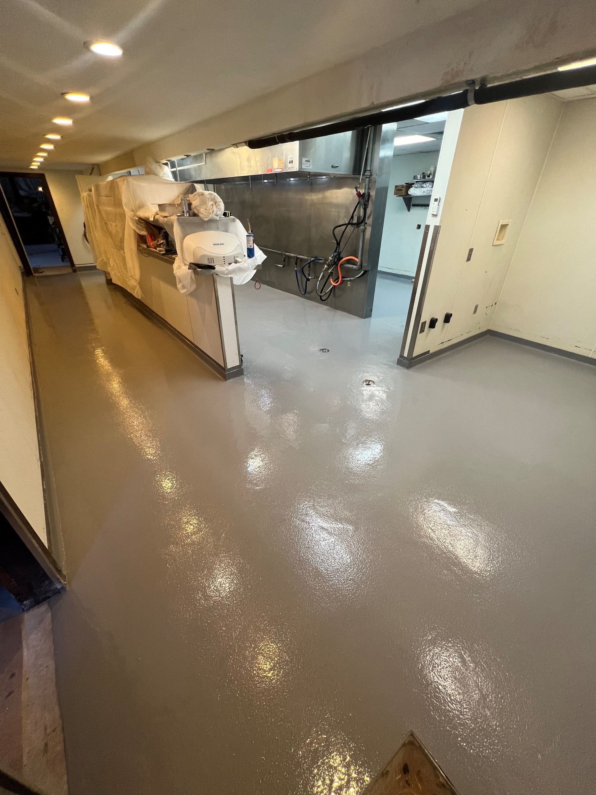 A wide, empty room with a gray floor and bright overhead lights. A white counter is in the middle of the room.