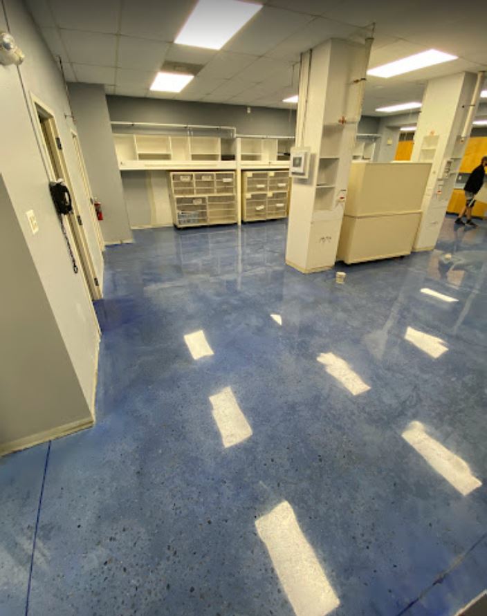 Blue epoxy floor in an empty room with white walls and storage. Bright light reflects off the floor.