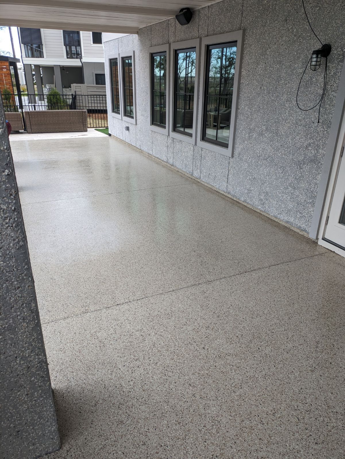 A covered outdoor area with a glossy speckled floor and wall. Windows line the wall, offering a view outside.