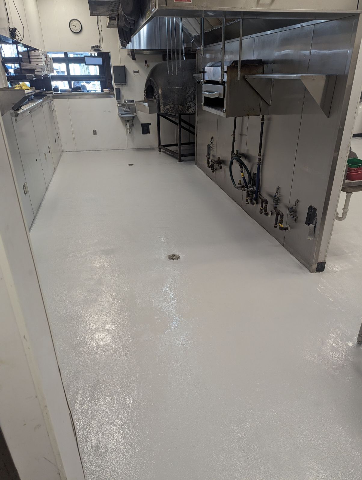 A commercial kitchen with a gray, epoxy-coated floor. Stainless steel equipment lines the walls.