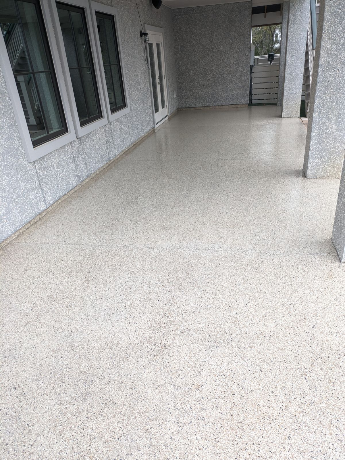 A porch with a speckled, light-colored concrete floor and matching wall finish. Several windows and doors are visible.