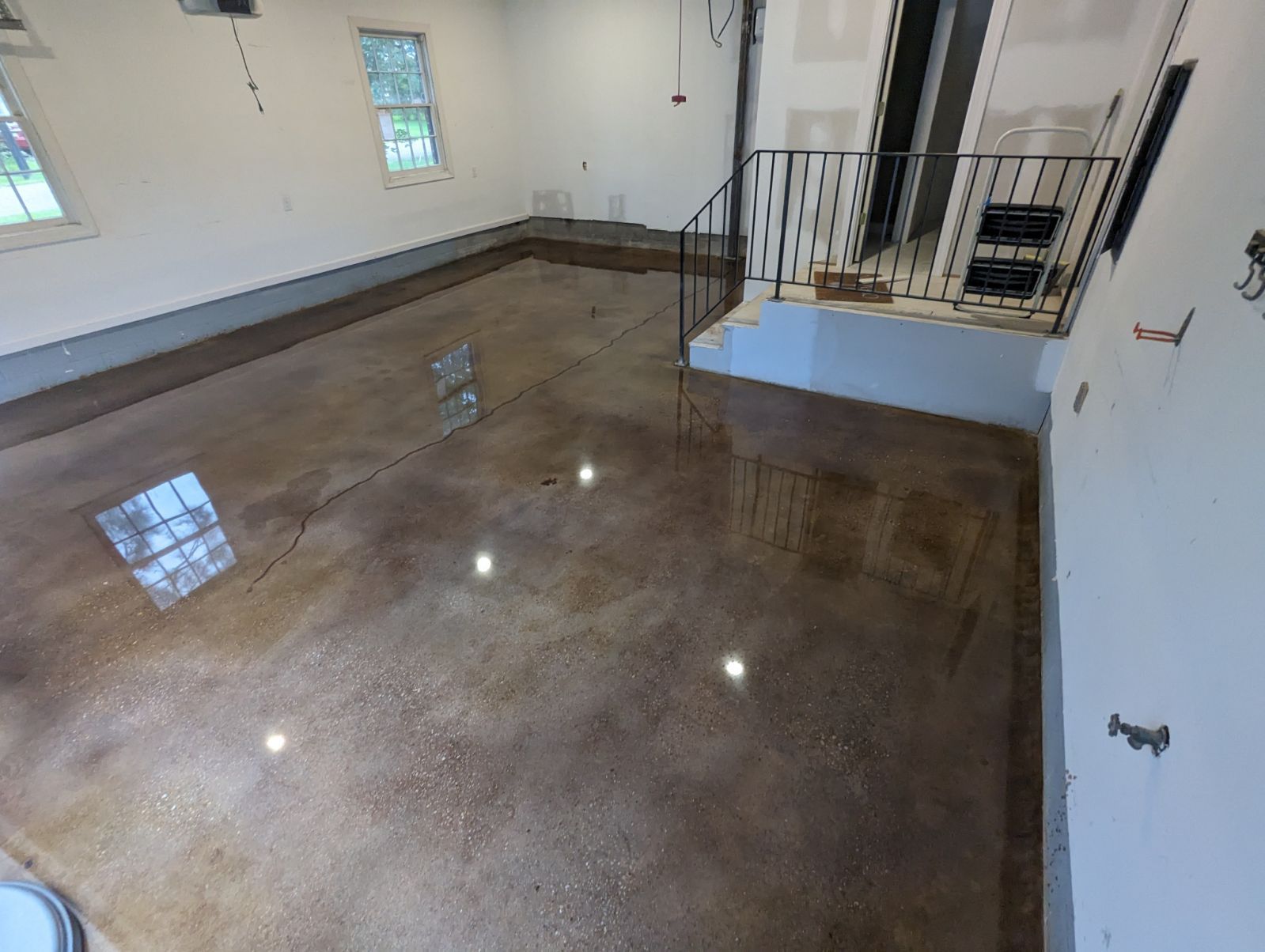 A spacious garage with a polished brown floor reflecting interior lights, two windows, and a staircase.