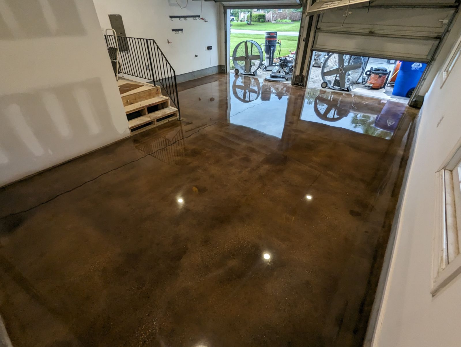 Brown epoxy-coated garage floor reflecting the open garage door and surrounding objects. Stairs lead to a higher level.
