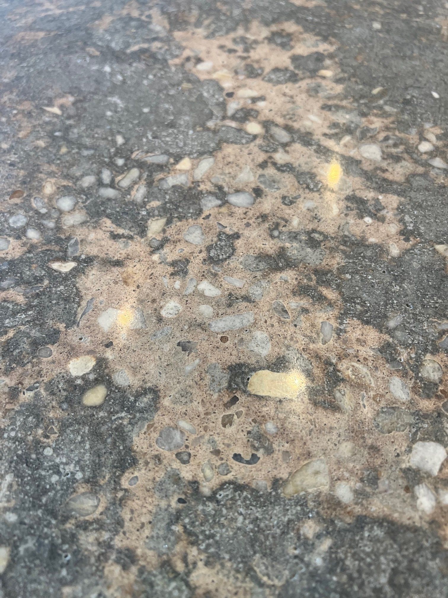Close-up of a speckled concrete surface, with gray and tan tones and exposed aggregate.