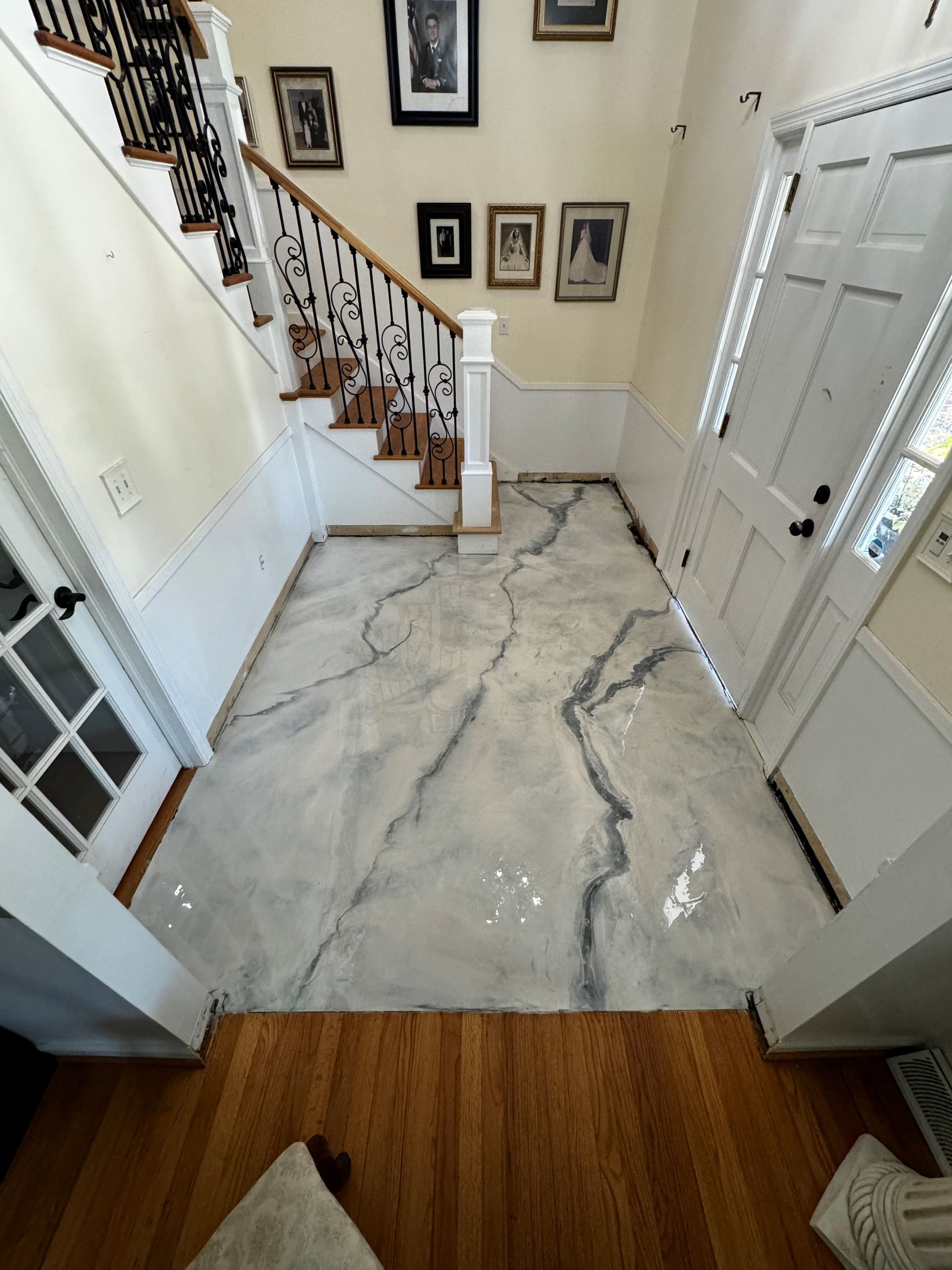 A hallway with a marble-effect floor, staircase, and framed photos. The front door is on the right.
