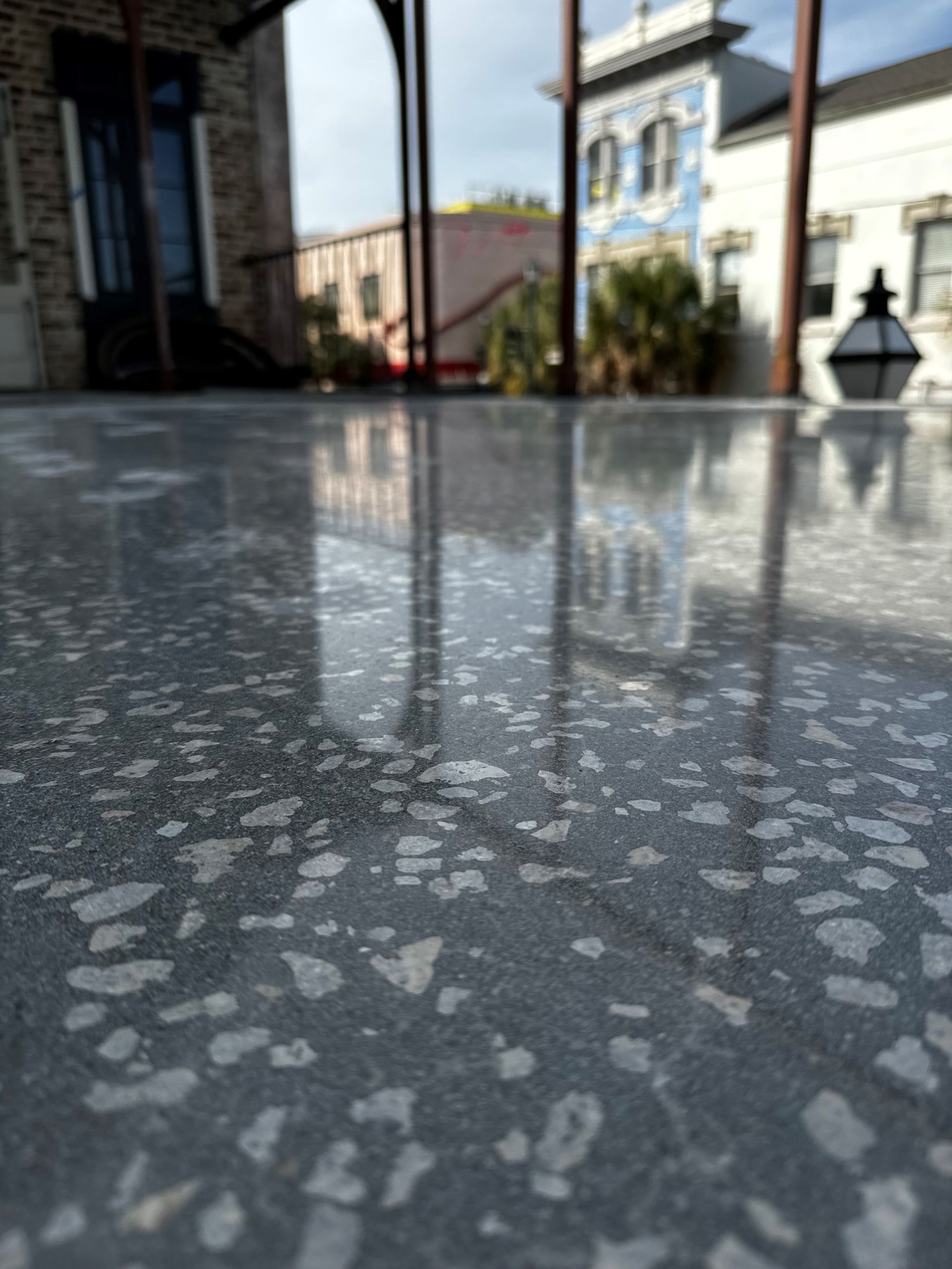 Polished concrete floor reflecting buildings and sky. Foreground is a close-up of the mottled gray surface.