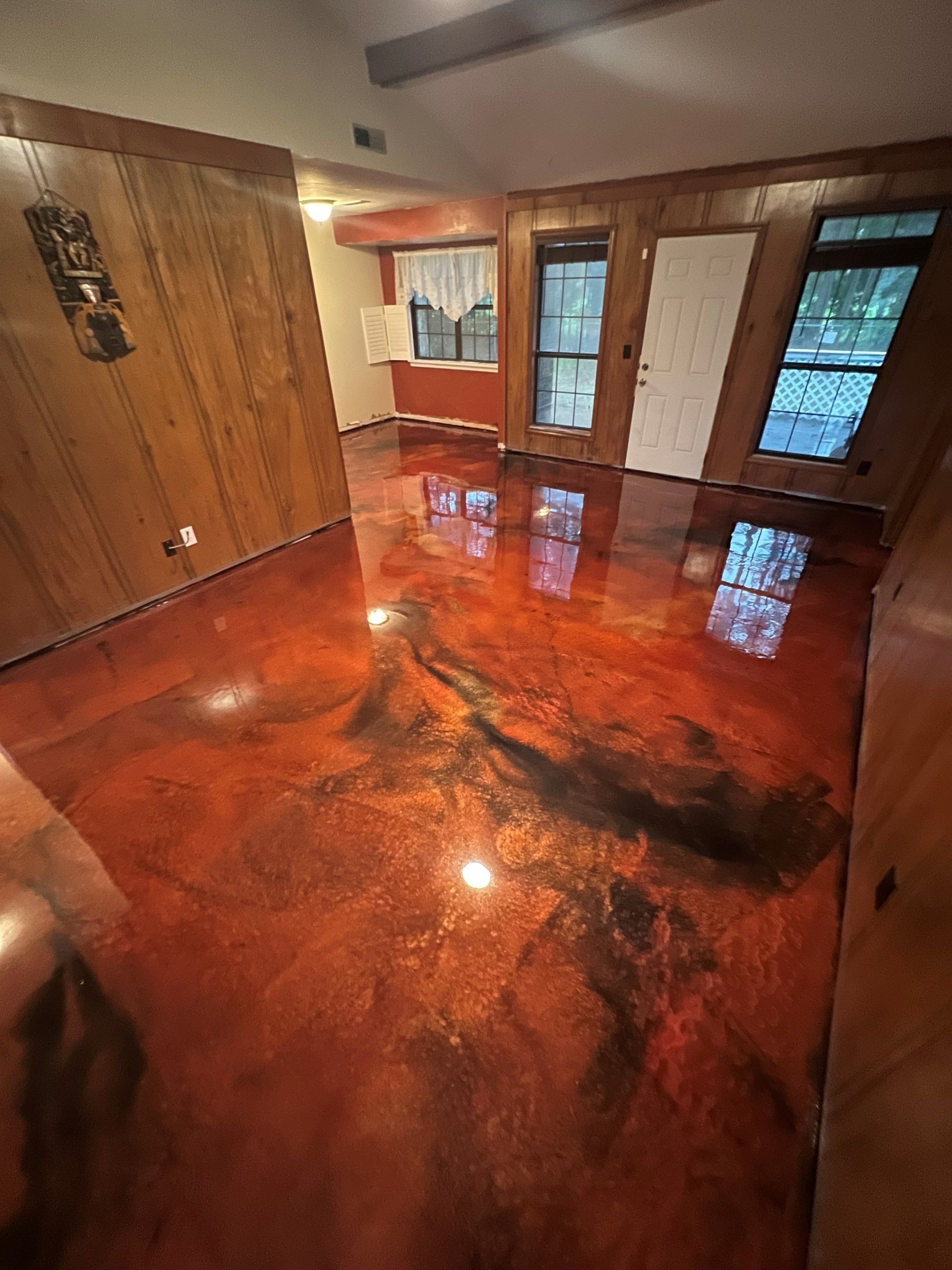 Room with a glossy, red and black metallic epoxy floor. The walls are wood paneling.