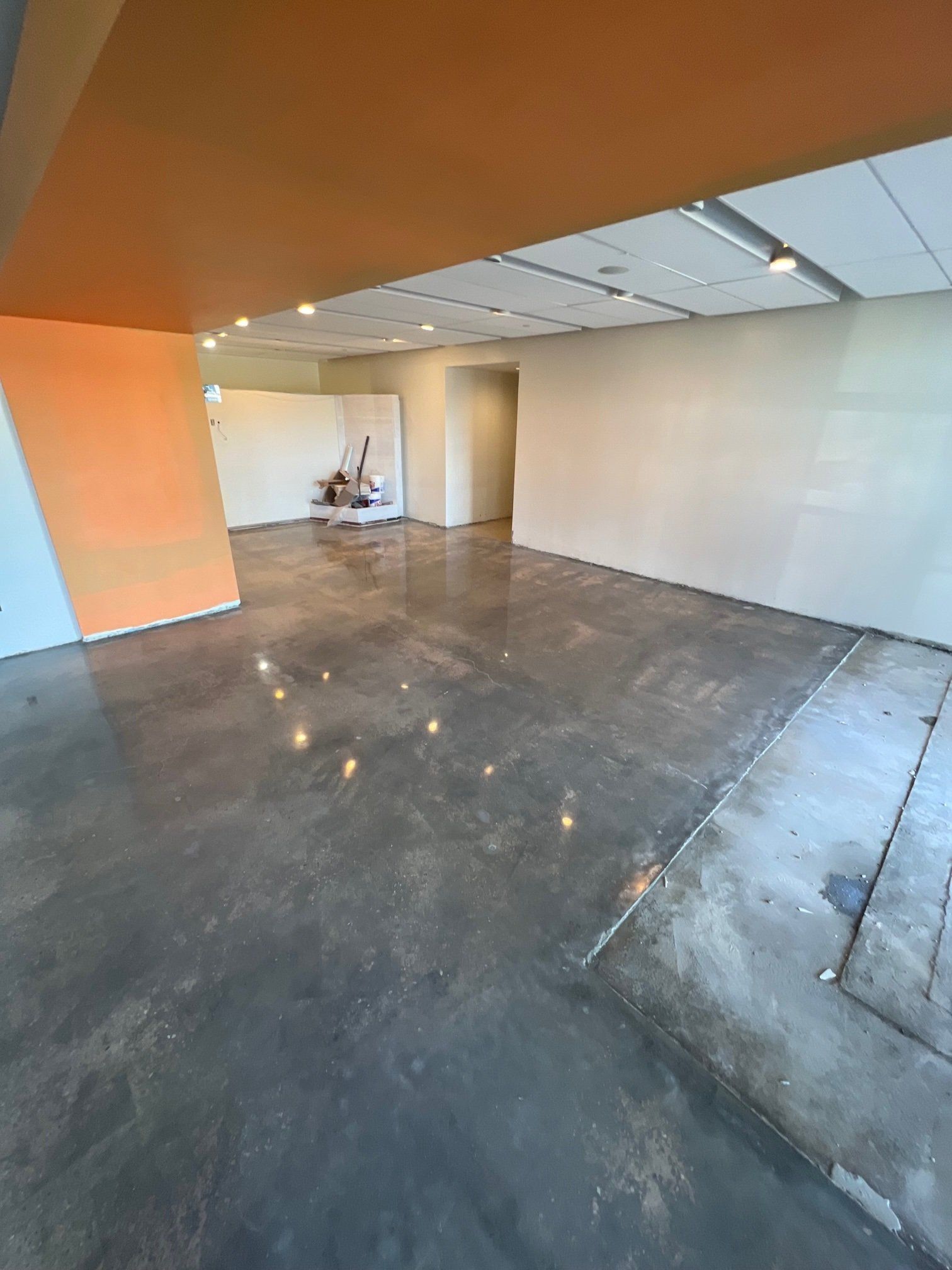 Empty room with polished concrete floor, orange and white walls, and recessed lighting.