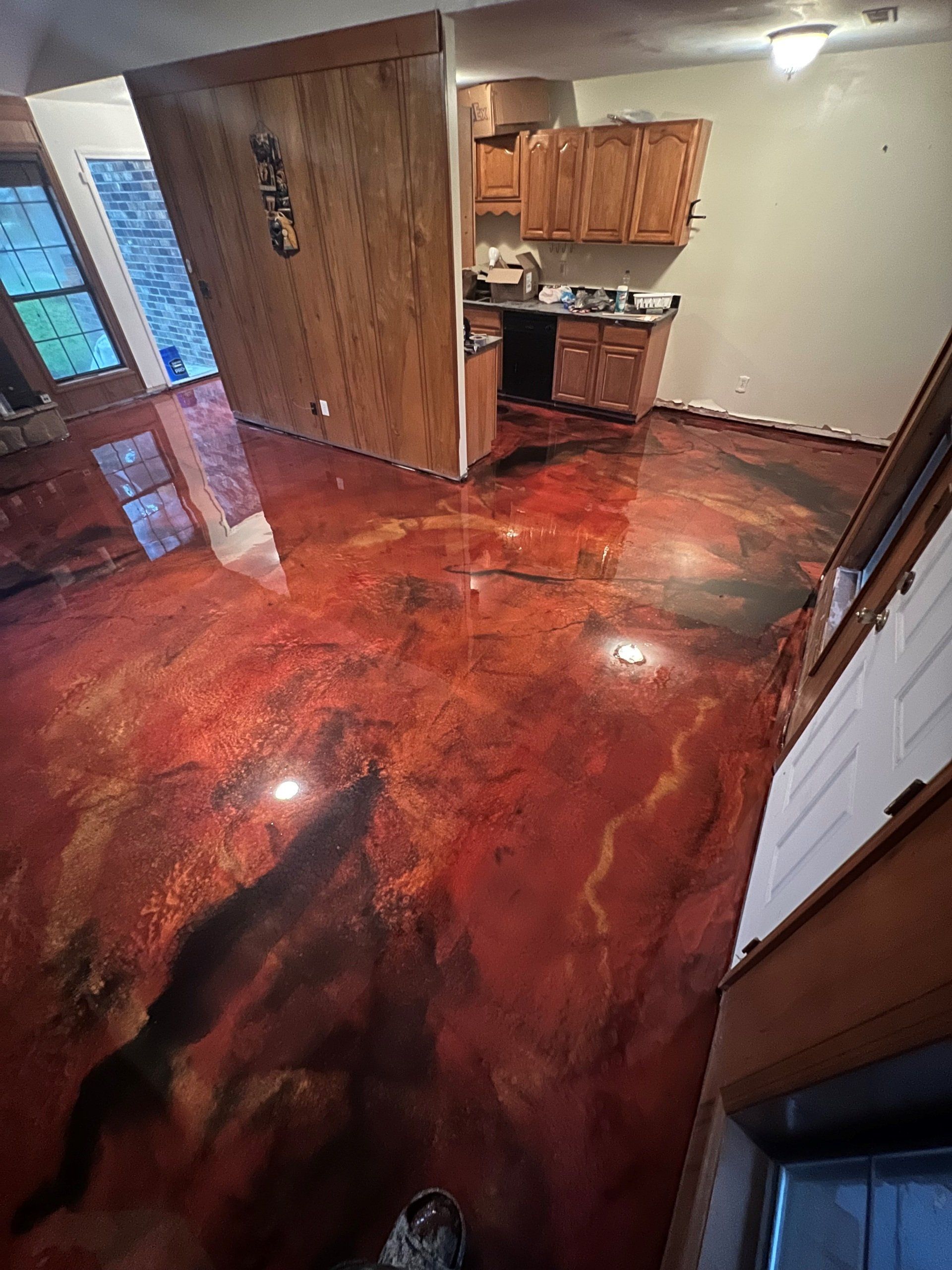 Interior view of a room with a red, marbled epoxy floor. Wooden cabinets and walls, and a partial view of a kitchen.