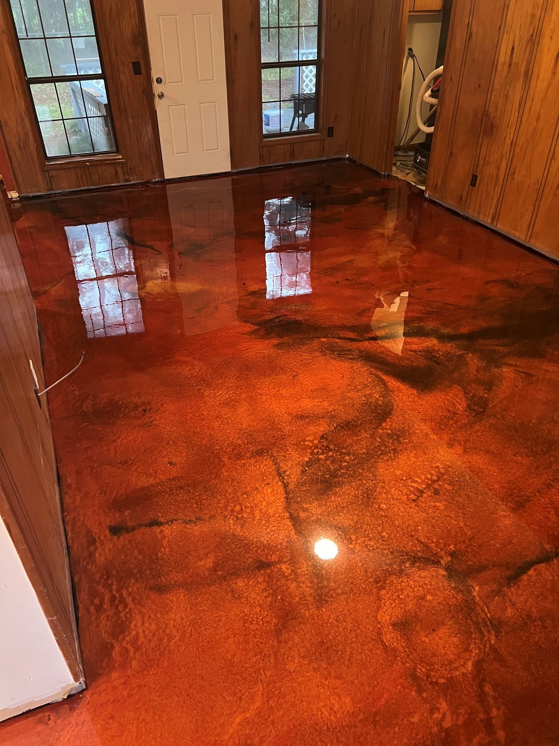 Shiny, metallic orange epoxy floor with dark accents, reflecting light in a room with windows and a door.