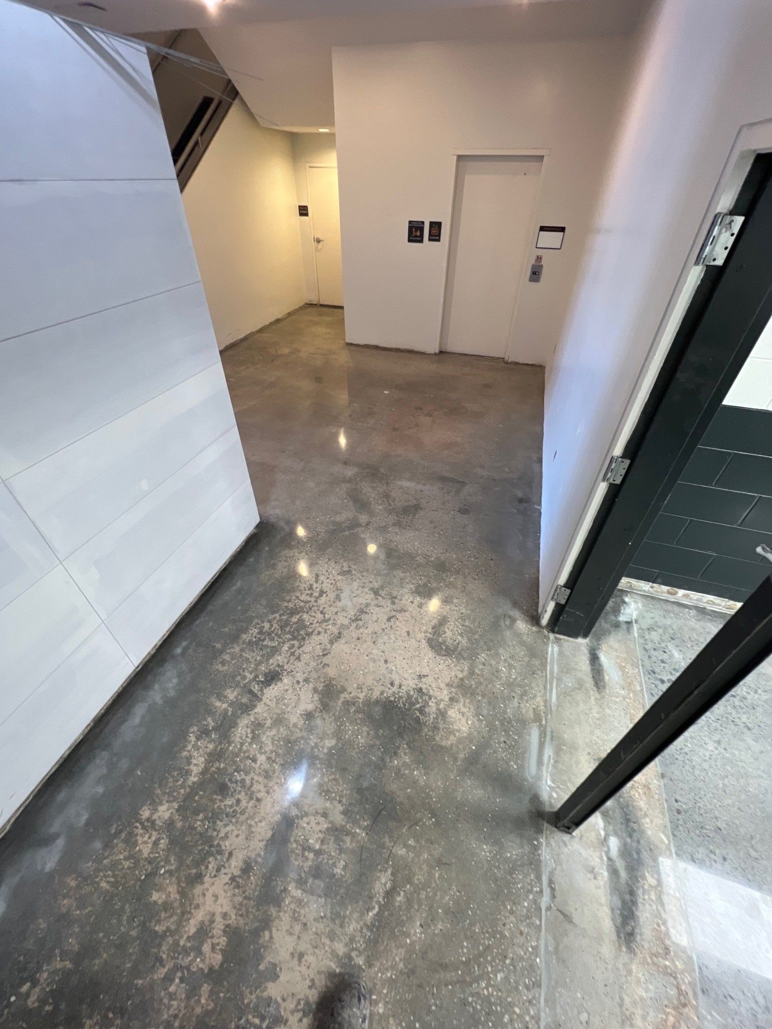 A hallway with polished concrete floors. A white door and a staircase are visible, along with a black door frame.
