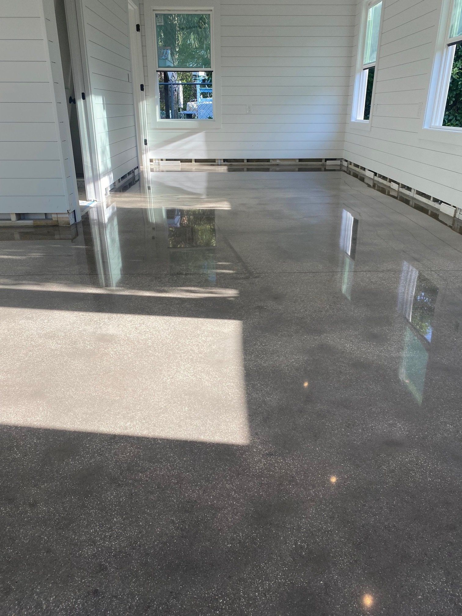 Polished concrete floor reflecting sunlight in a white-walled room with windows.