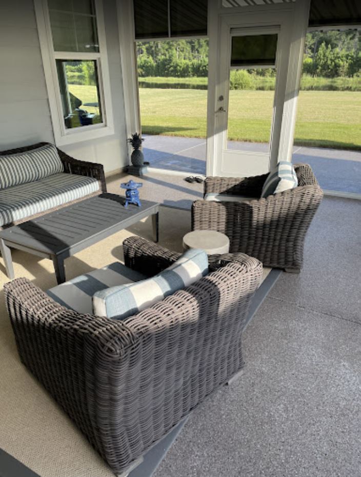 Outdoor patio with dark wicker furniture, a gray table, and views of a grassy field through open spaces.