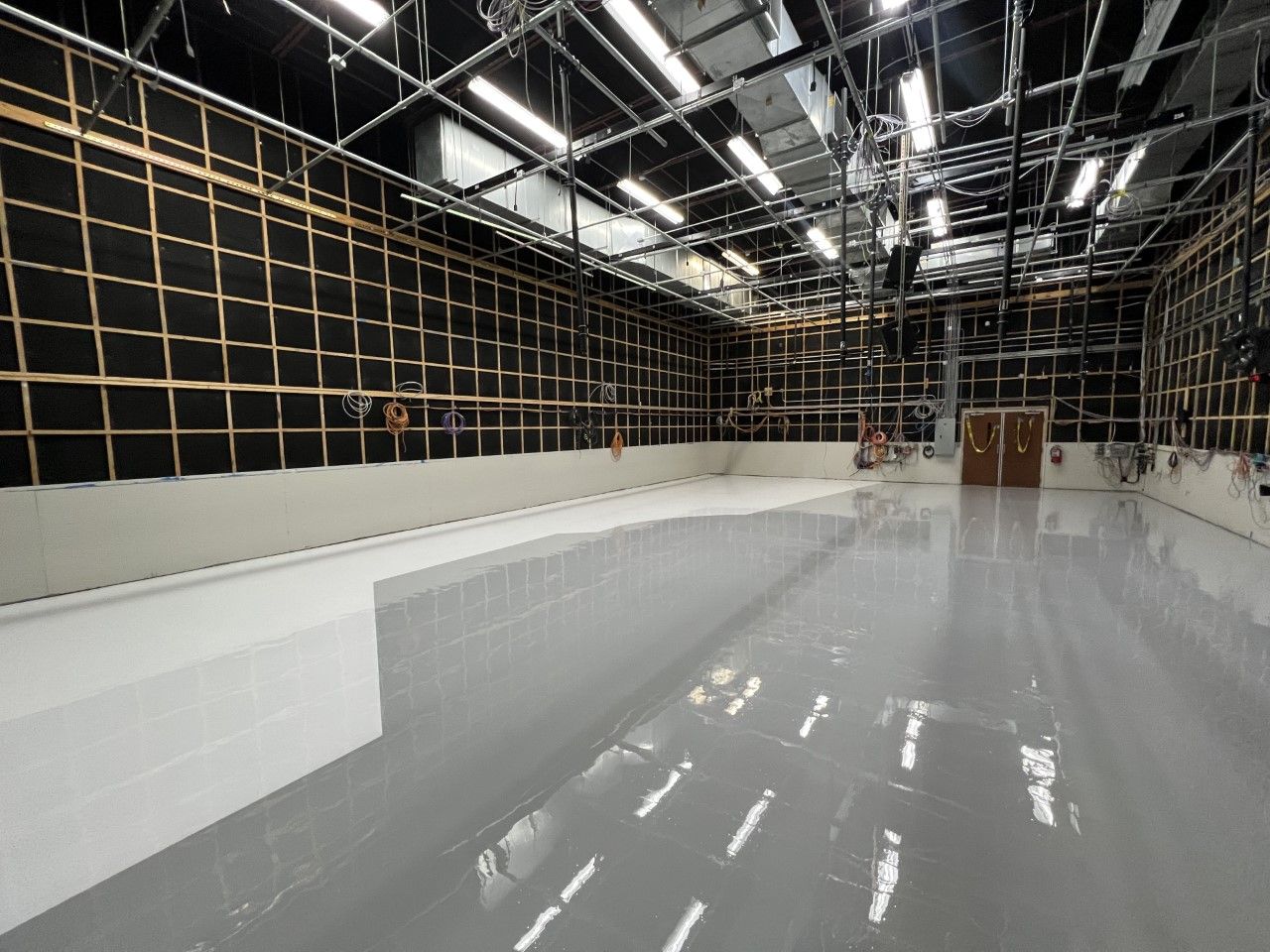 Empty soundstage with glossy gray floor and black acoustic panels on the walls; overhead lighting and equipment visible.