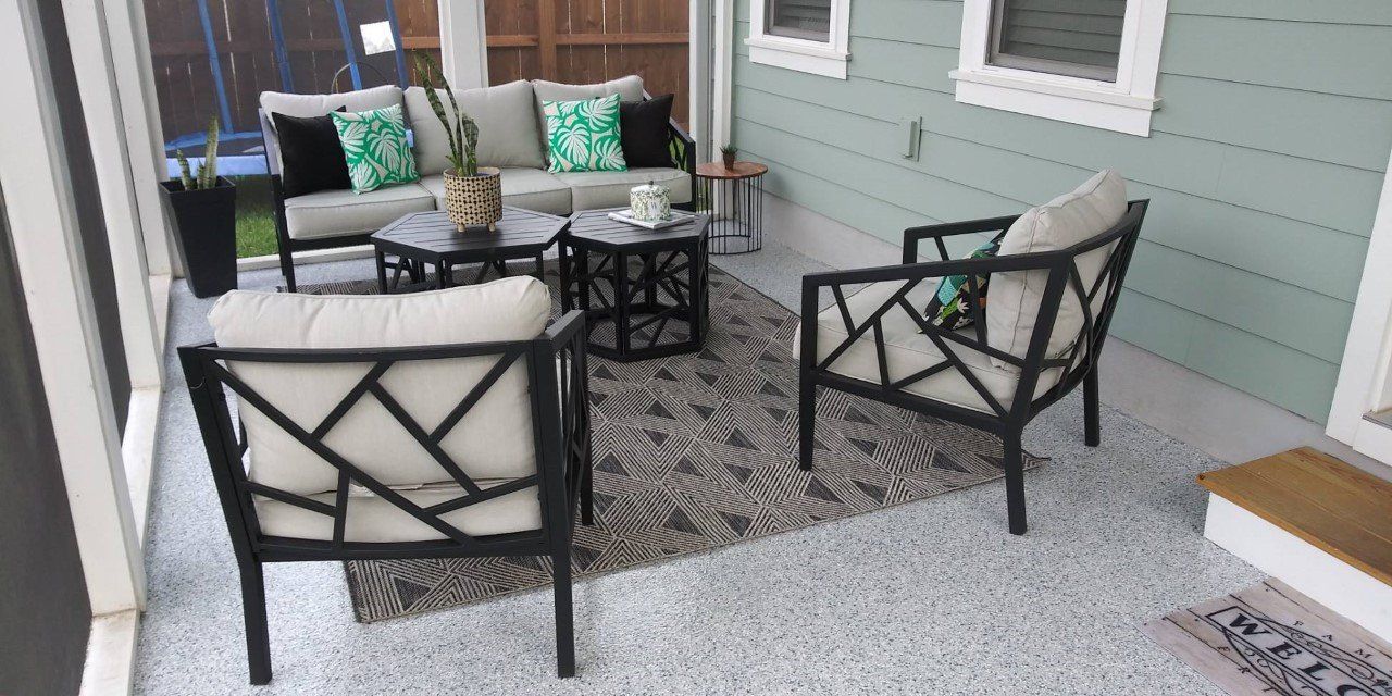 Outdoor patio seating area with gray sofa, two armchairs, and coffee tables on a patterned rug. The walls are mint green.
