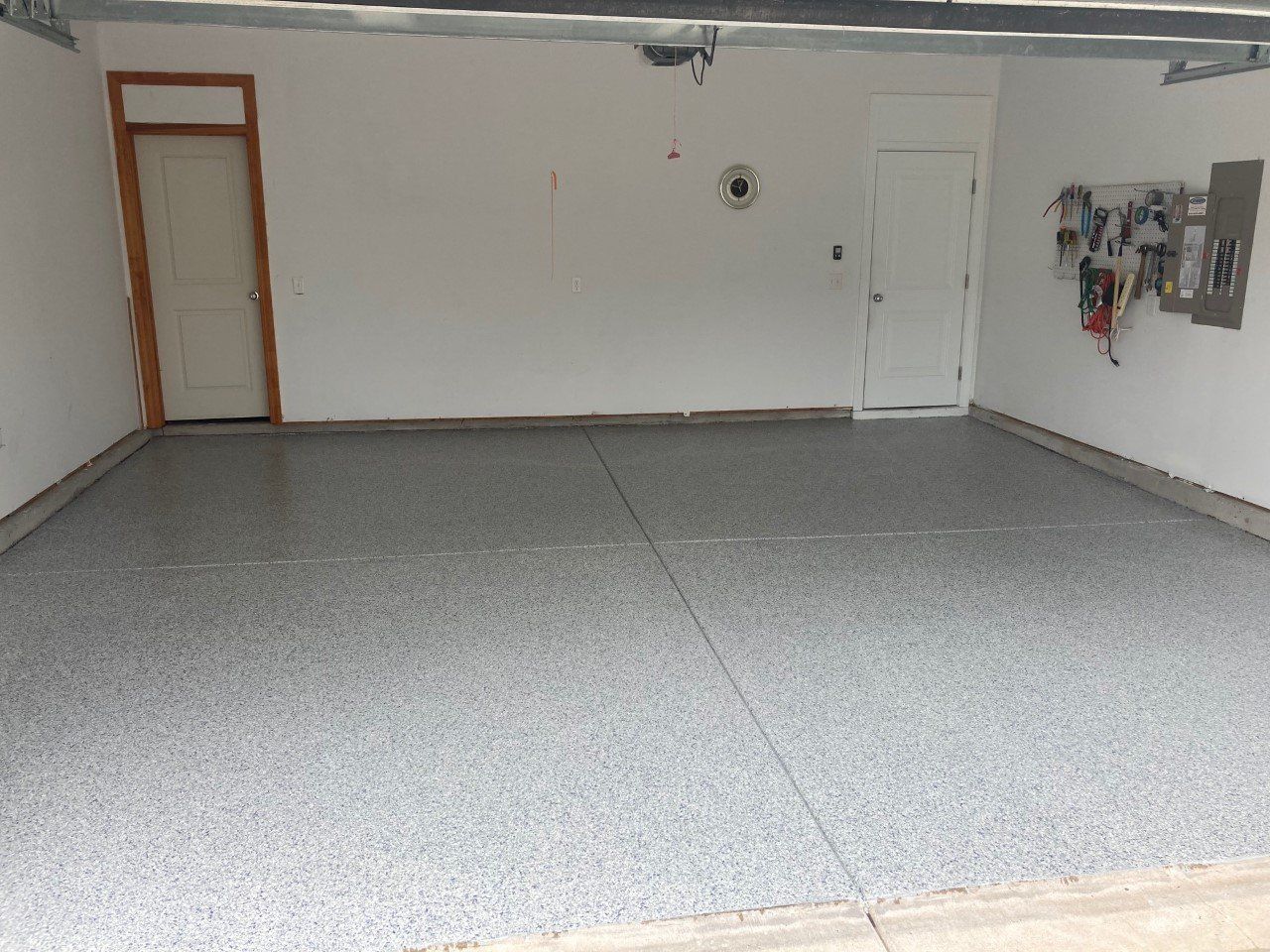 A newly painted garage with a speckled gray floor, white walls, and two doors.