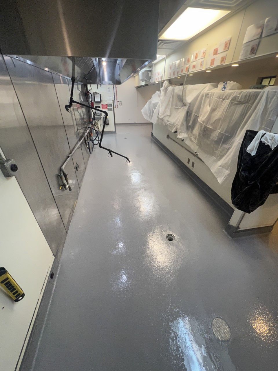 A commercial kitchen with gray epoxy floors, stainless steel fixtures, and covered appliances.