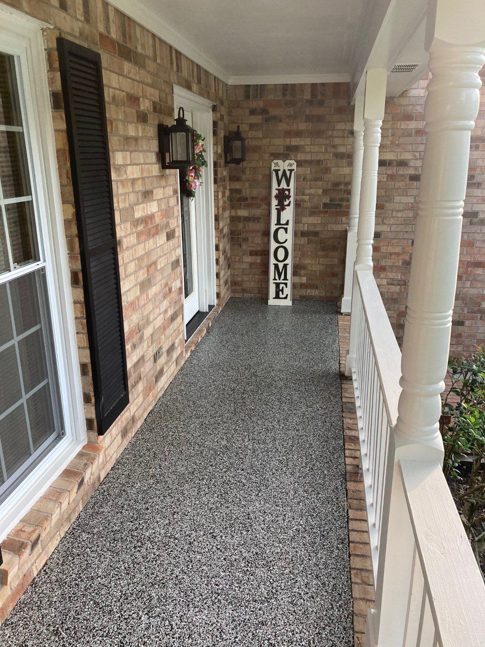A covered porch with a brick wall, dark flooring, and a 