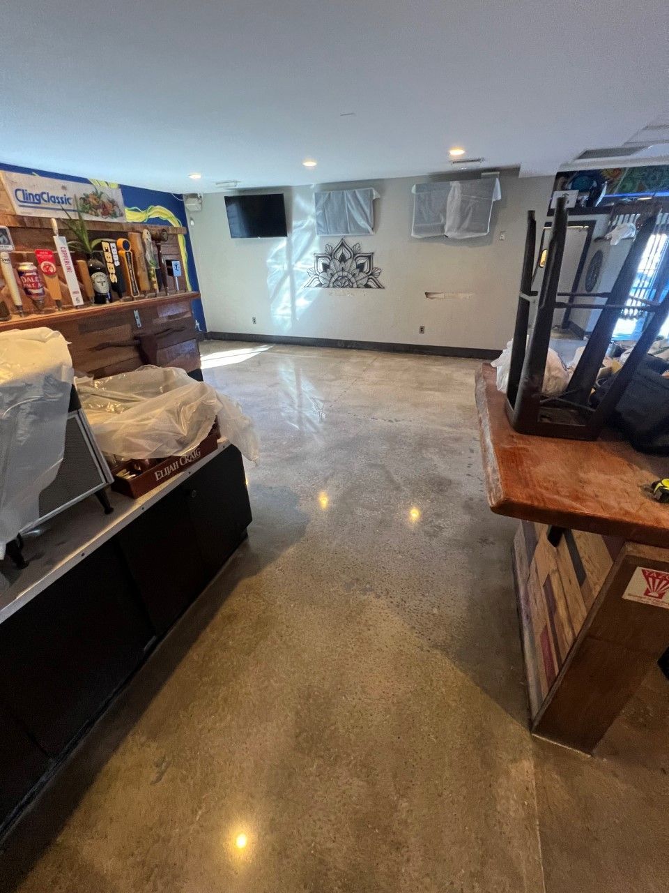 Polished concrete floor in a bar. A bar with turned-over stools, exposed wires, and a small TV is visible.