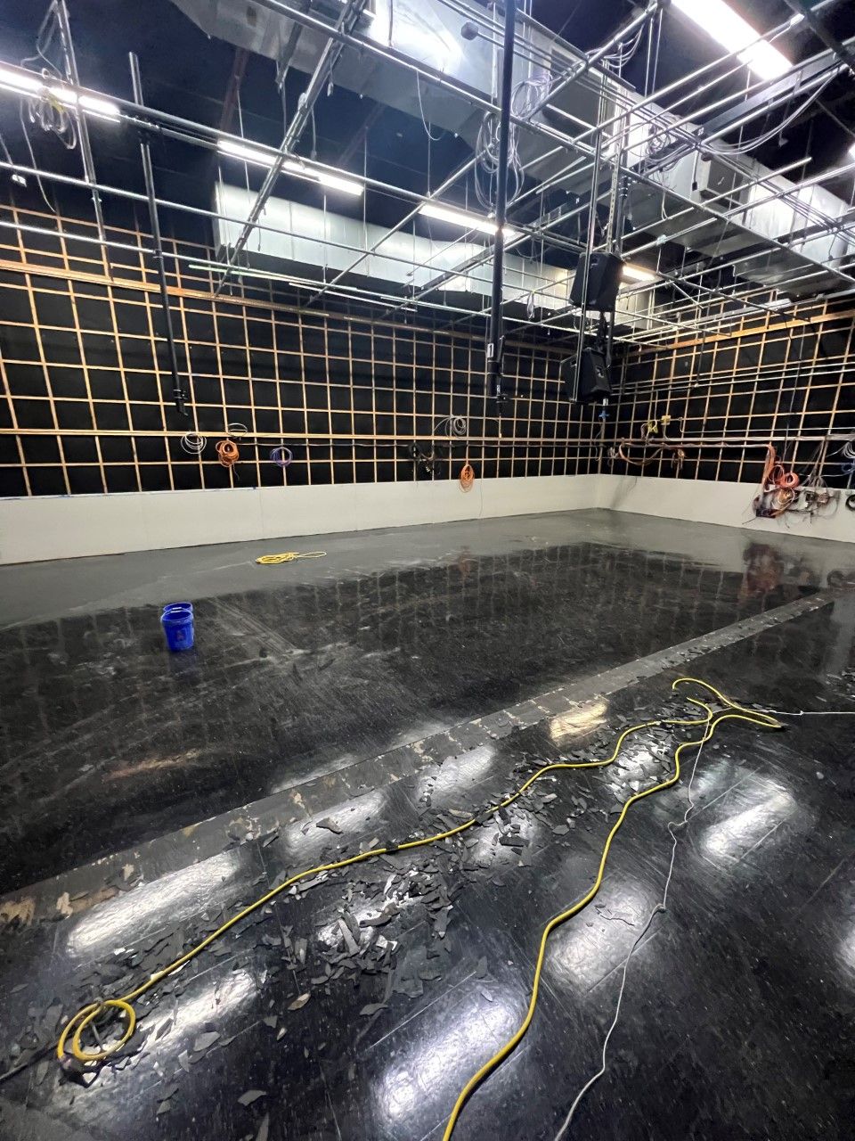 Interior of a large industrial space with a wet, reflective floor, exposed wall framework, and overhead beams.