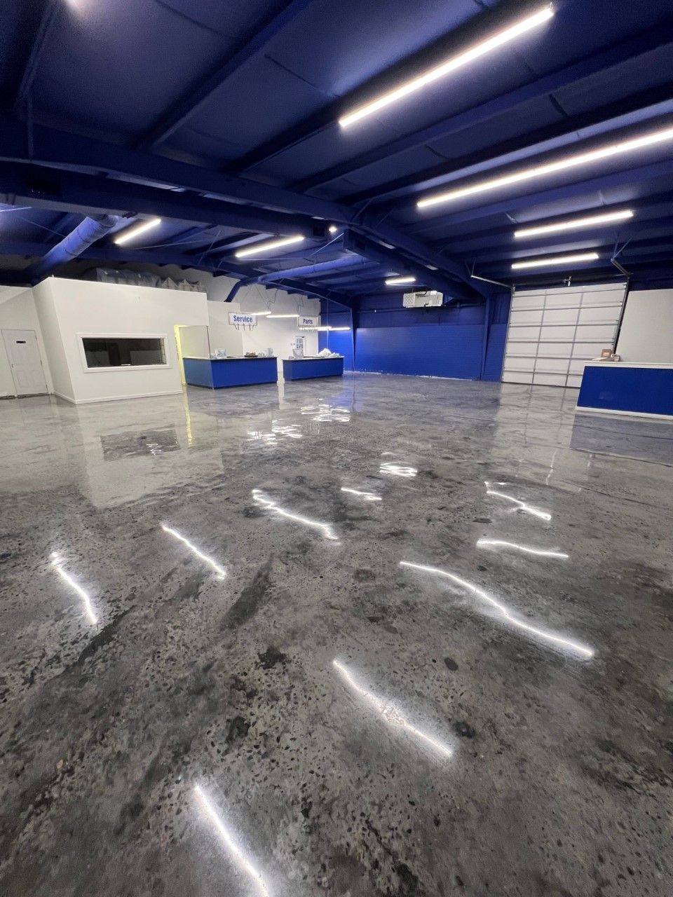 A wide, empty room with a gray floor and bright overhead lights. A white counter is in the middle of the room.