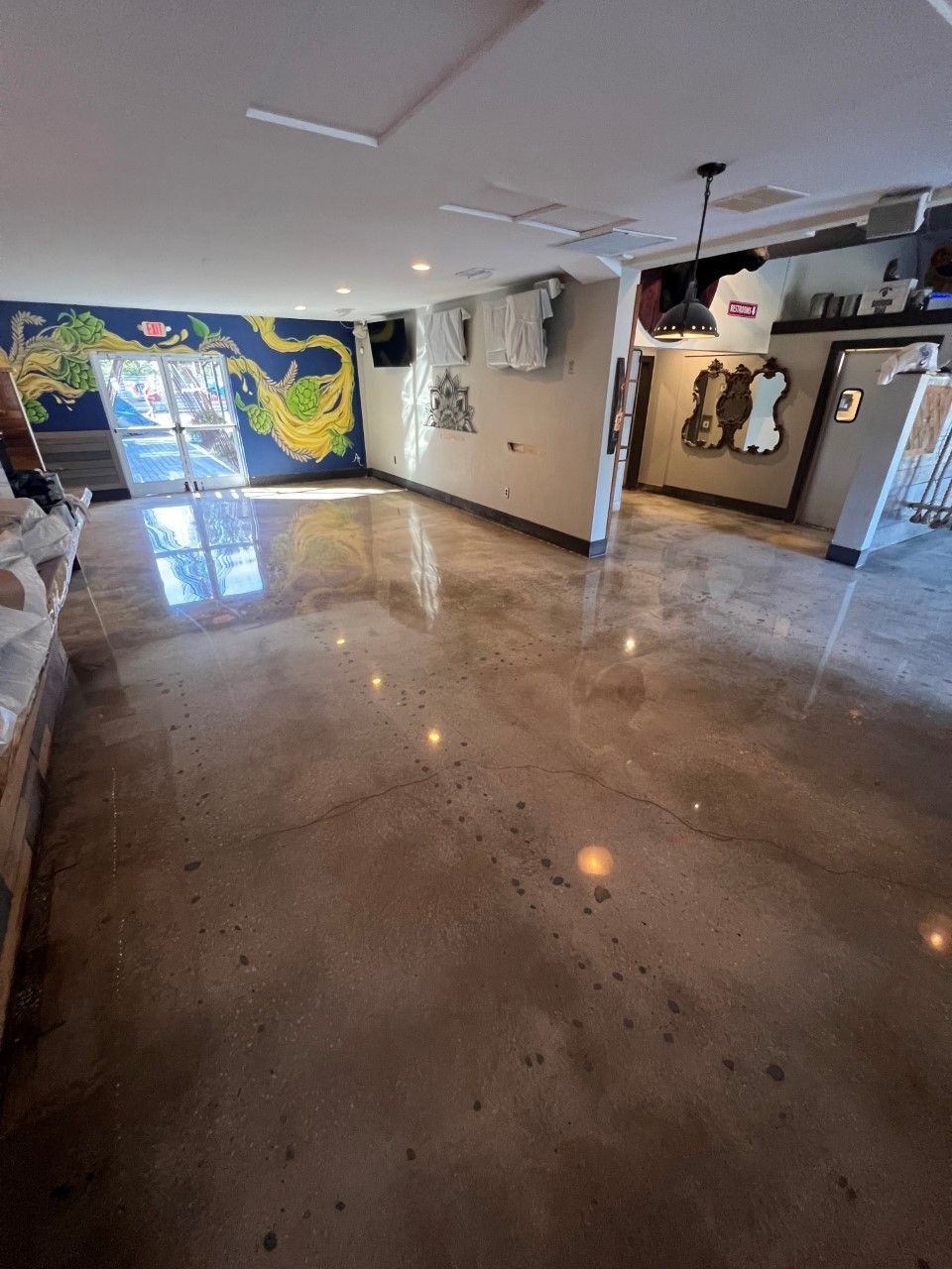 Empty interior with polished concrete floor, blue and white walls, and a mural. Bright lighting reflects off the floor.
